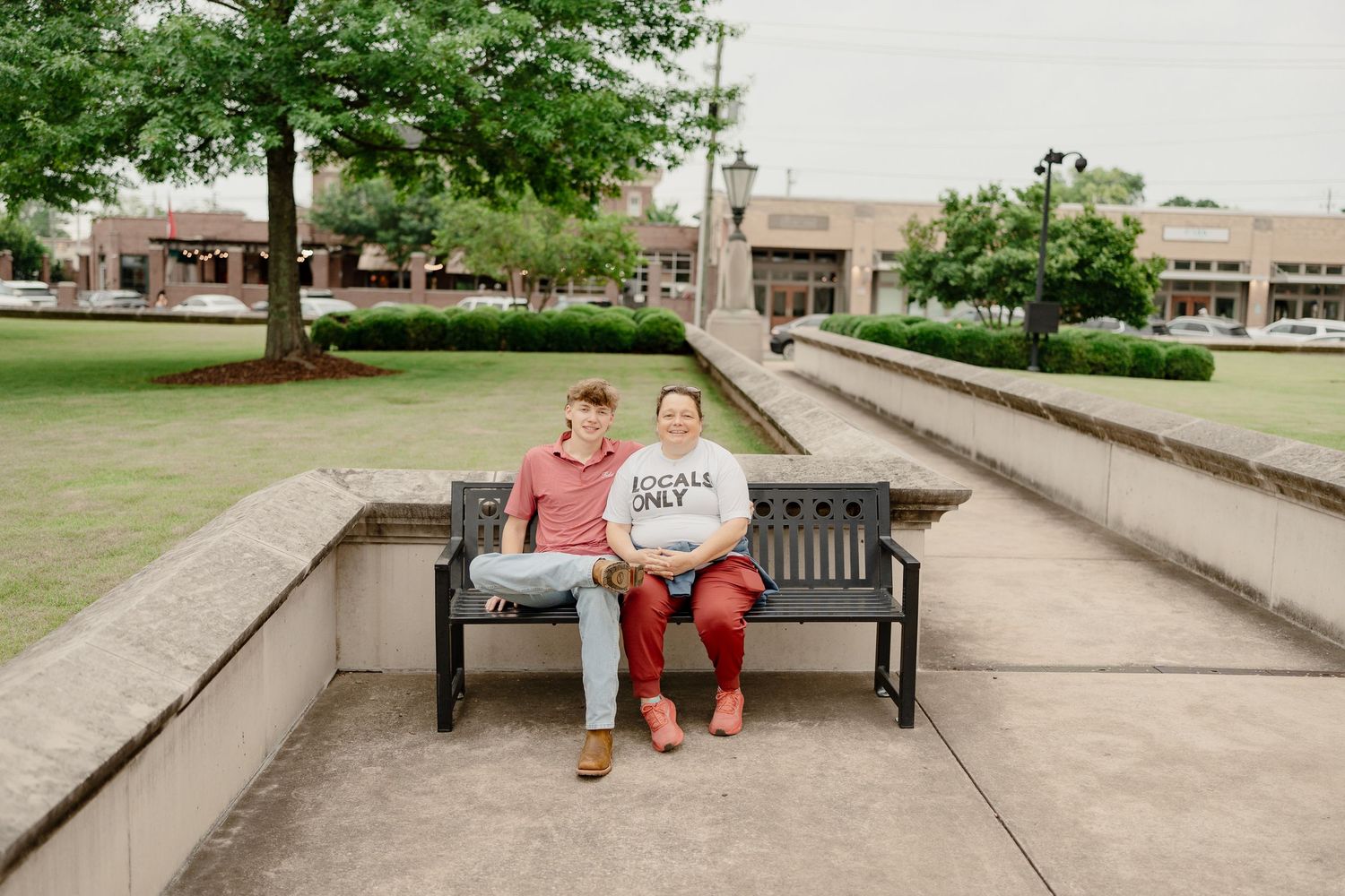 Two people share a moment on a bench in front of a campus building on a summer day.