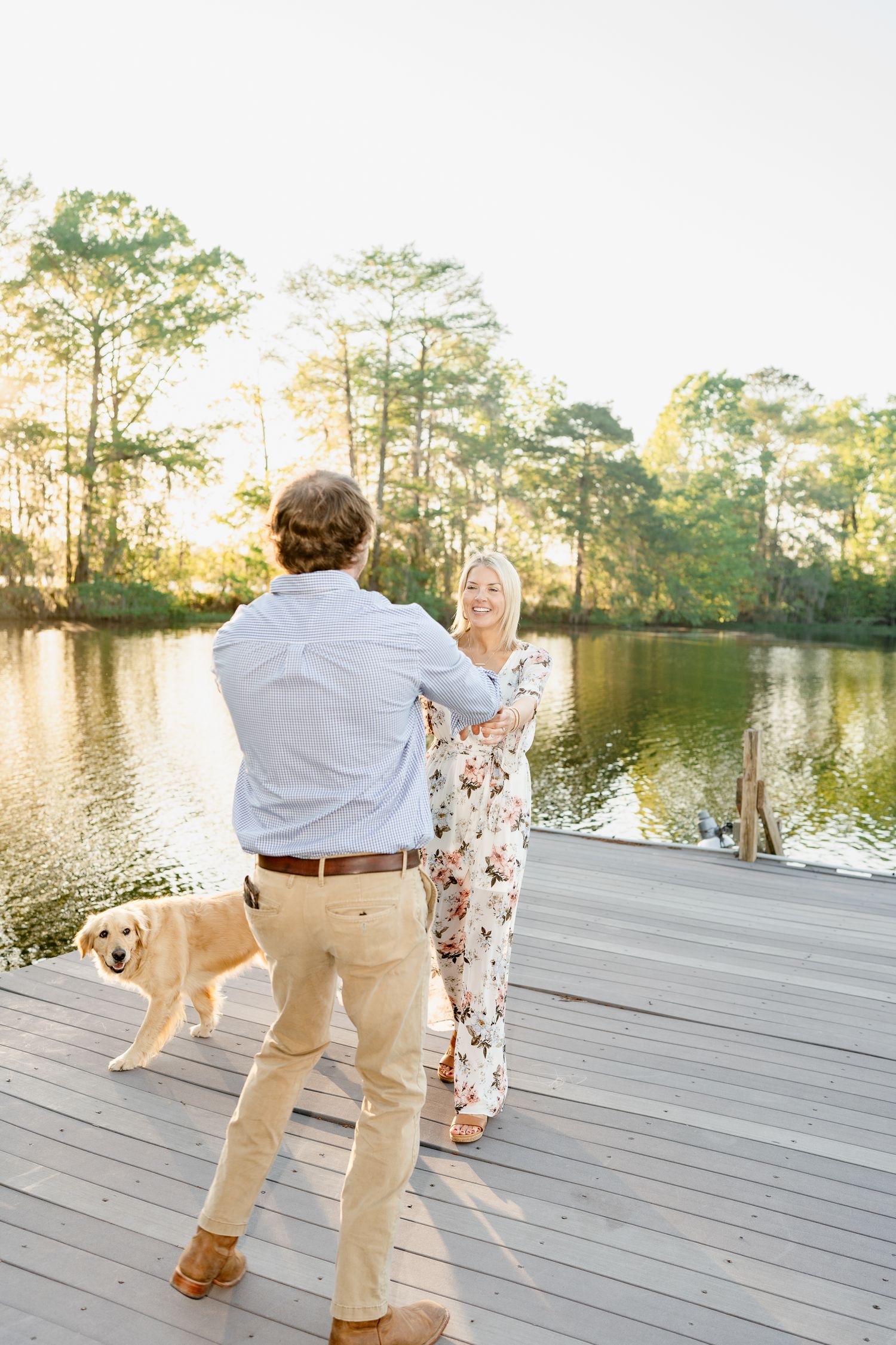 A couple dances on a wooden pier with a golden sunset and dog in the background.