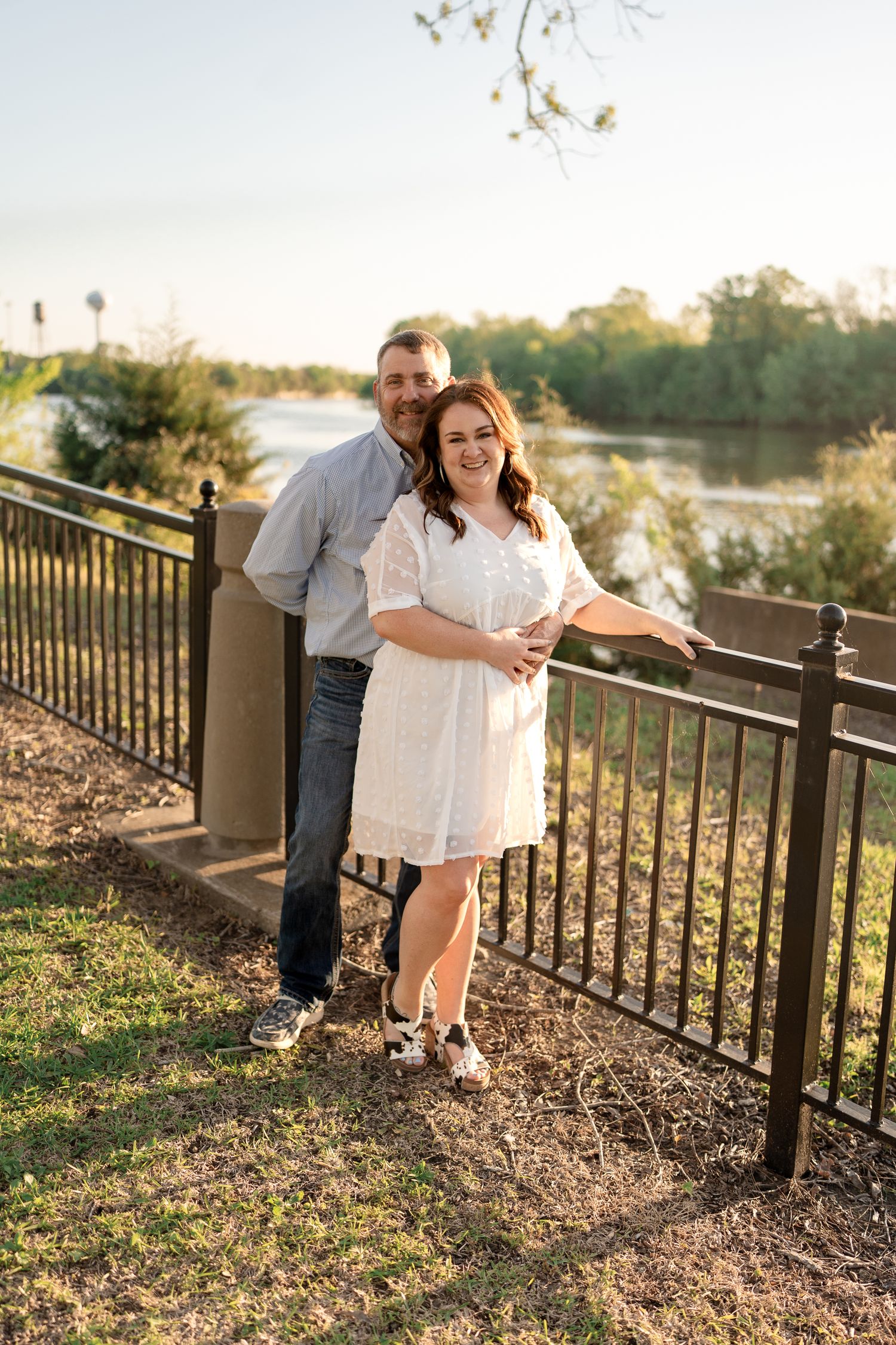 A couple posing together against an iron railing with a scenic water view.