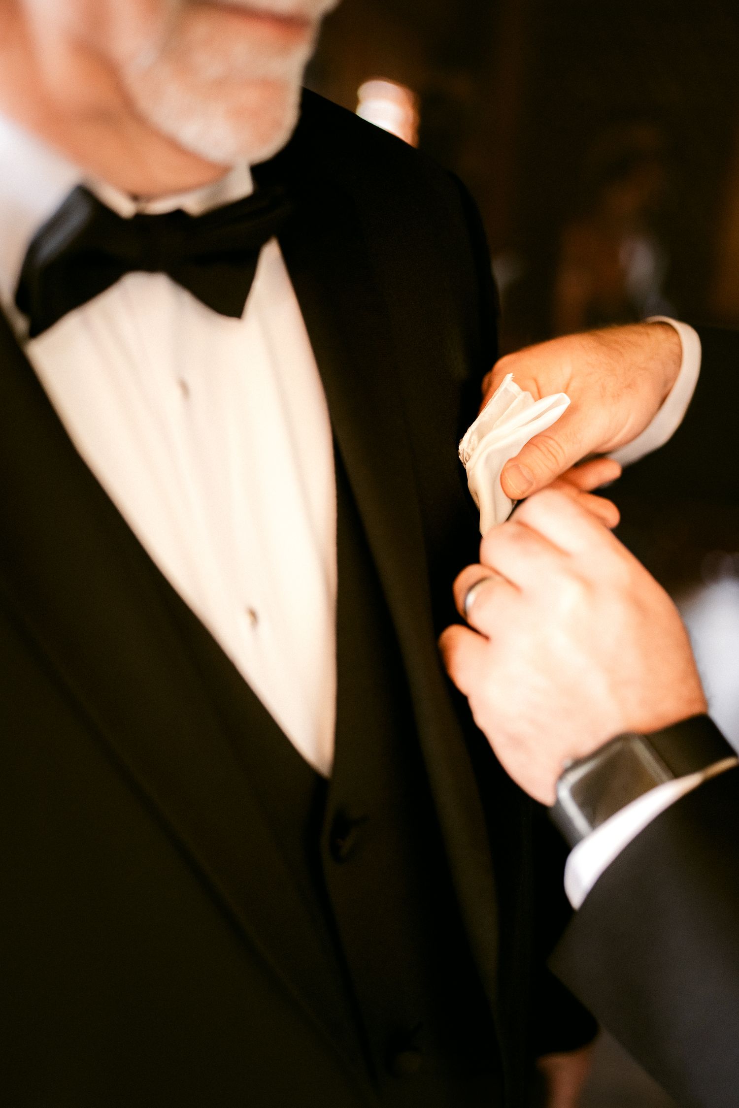 Close-up shot of hands adjusting a black bow tie on a formal tuxedo.
