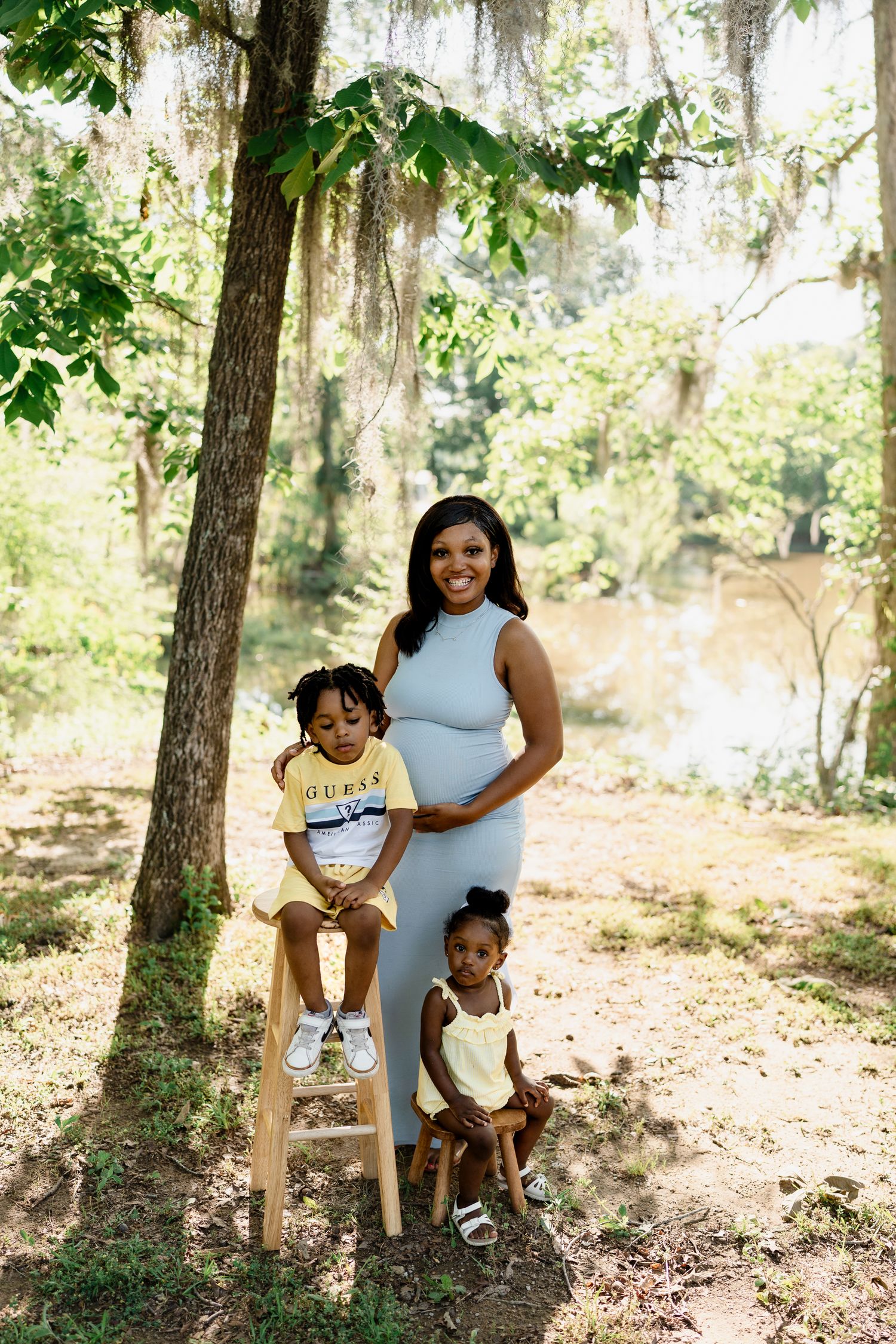 Family photoshoot in scenic wooded area with sunlight filtering through trees.