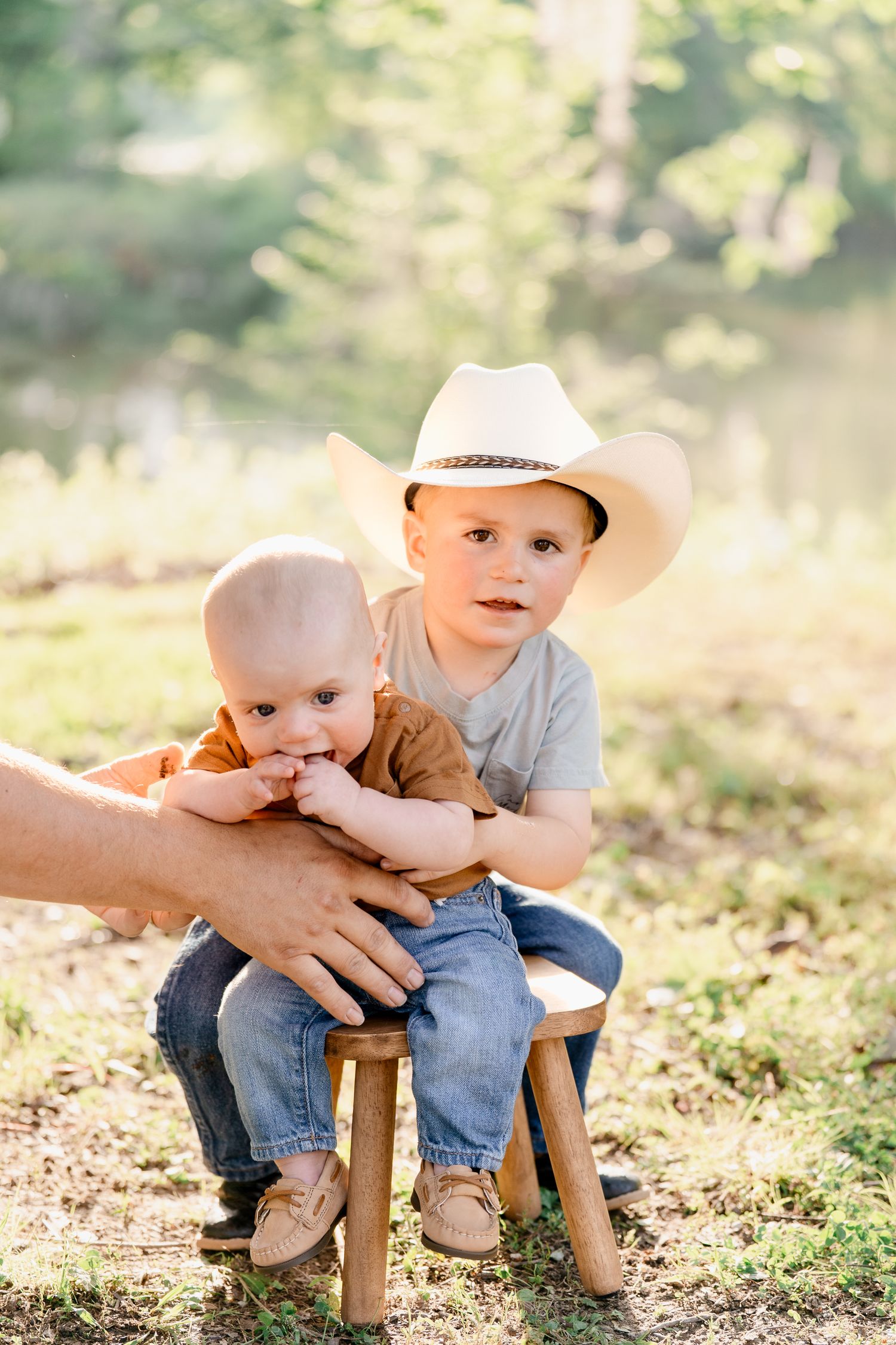Young child sits on wooden stool during rustic outdoor photo session.
