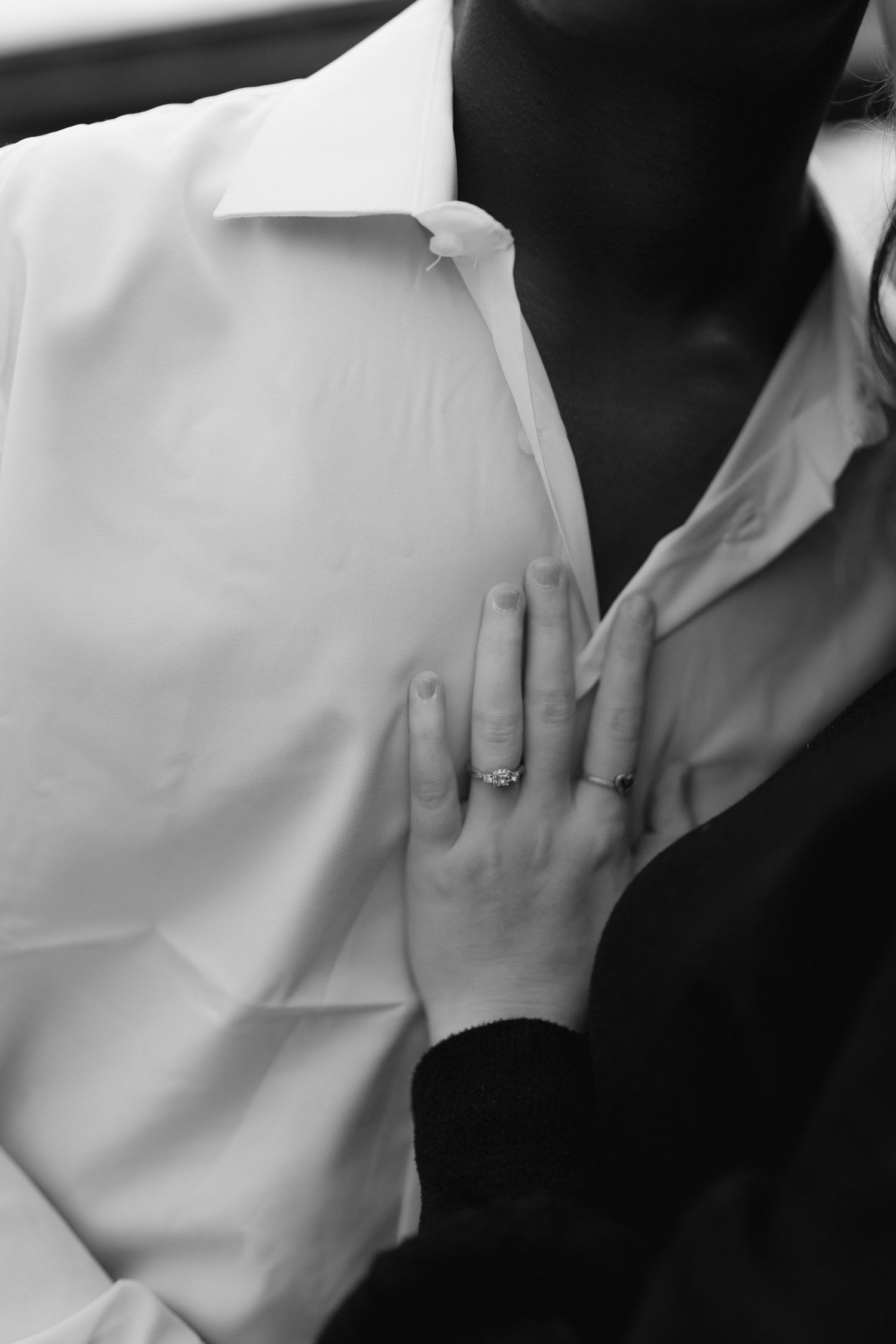 Black and white close-up of a woman's hand with an engagement ring resting on a man's white dress shirt.