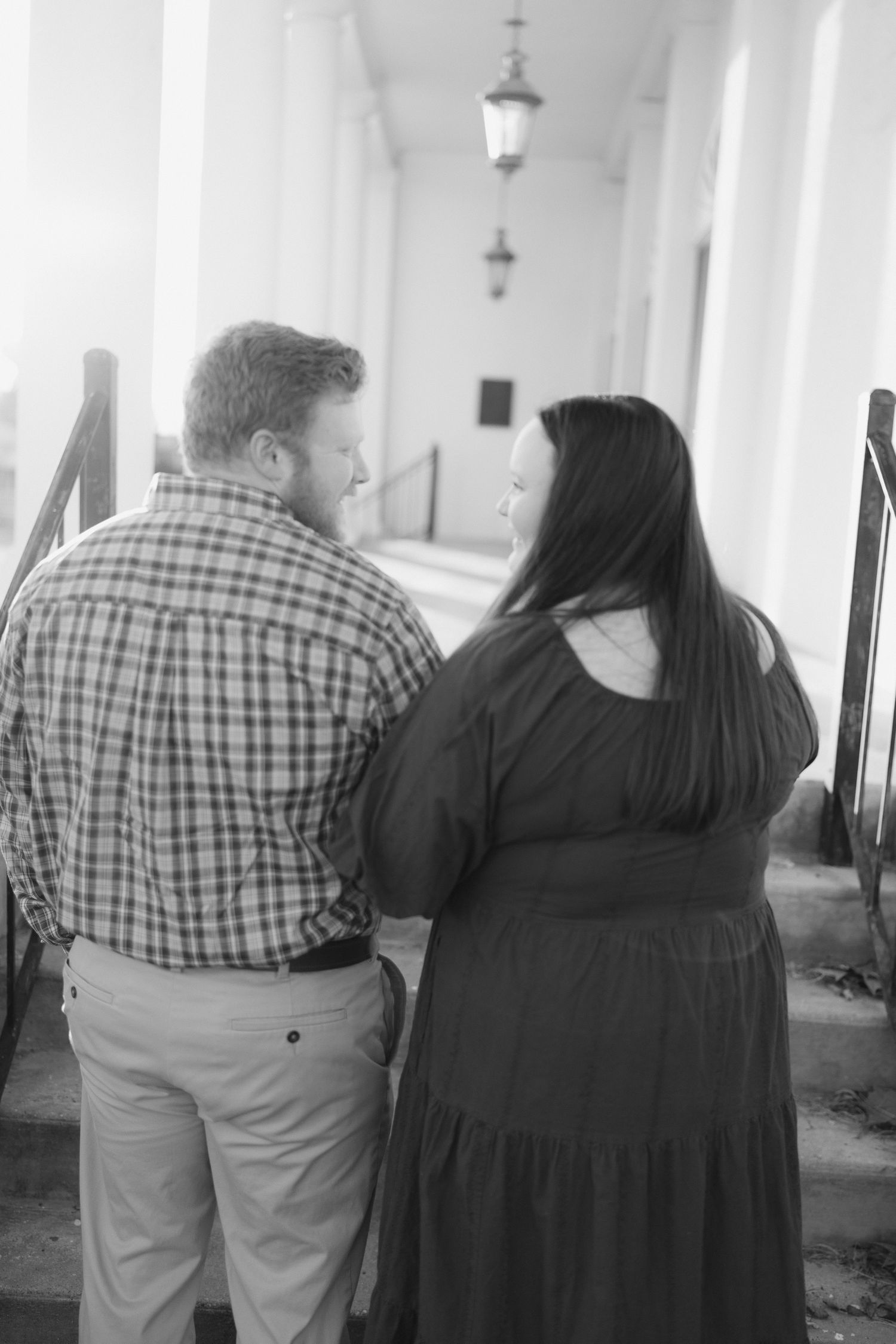 Black and white rear view of couple sharing a moment on steps of a columned historic building.