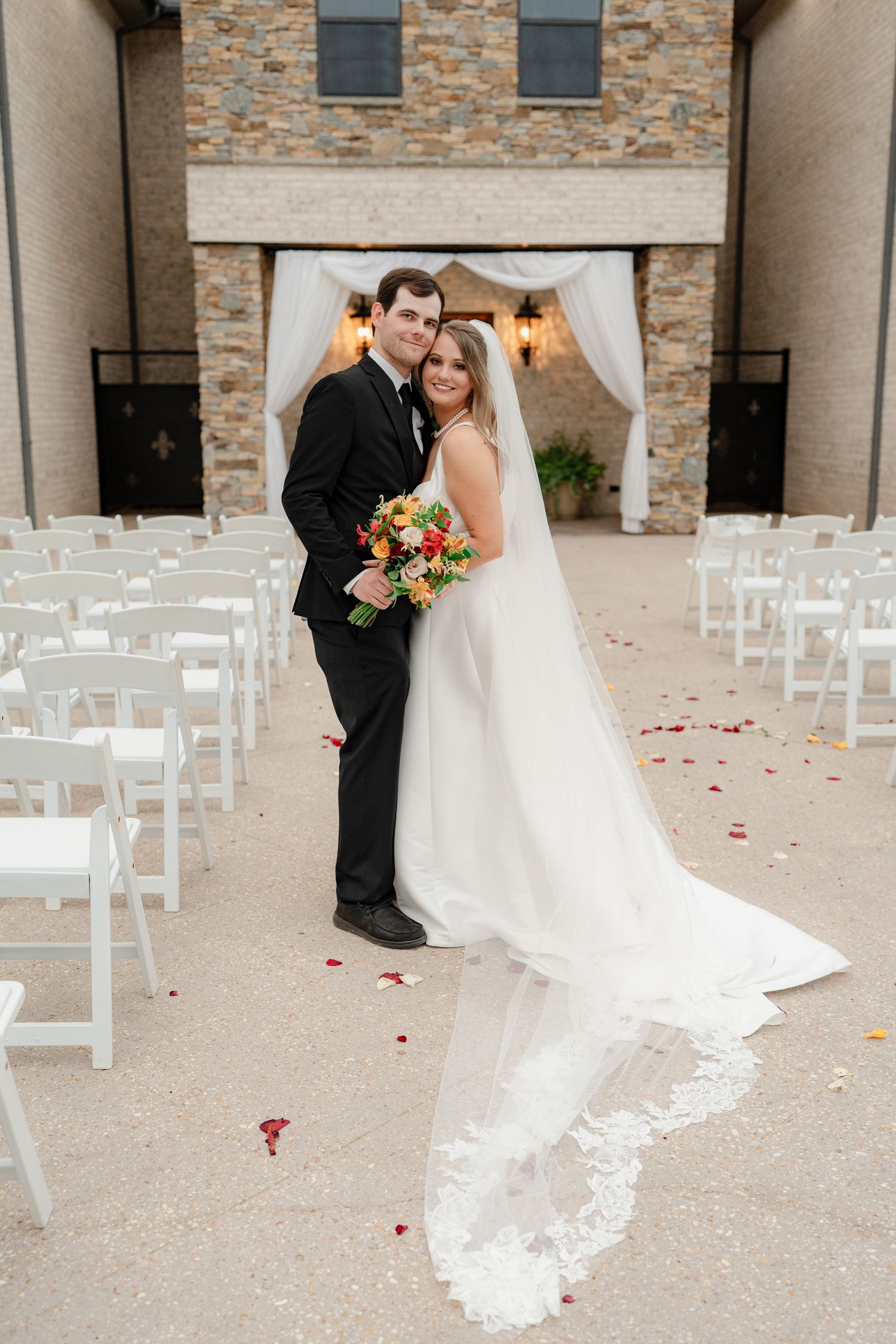 Wedding couple shares intimate moments in front of stone venue with scattered rose petals.