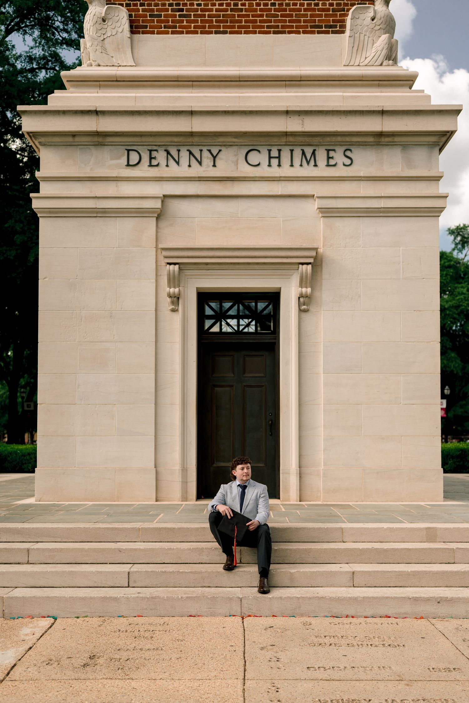 Young man in suit sitting on steps of Denny Chimes monument at University of Alabama campus.