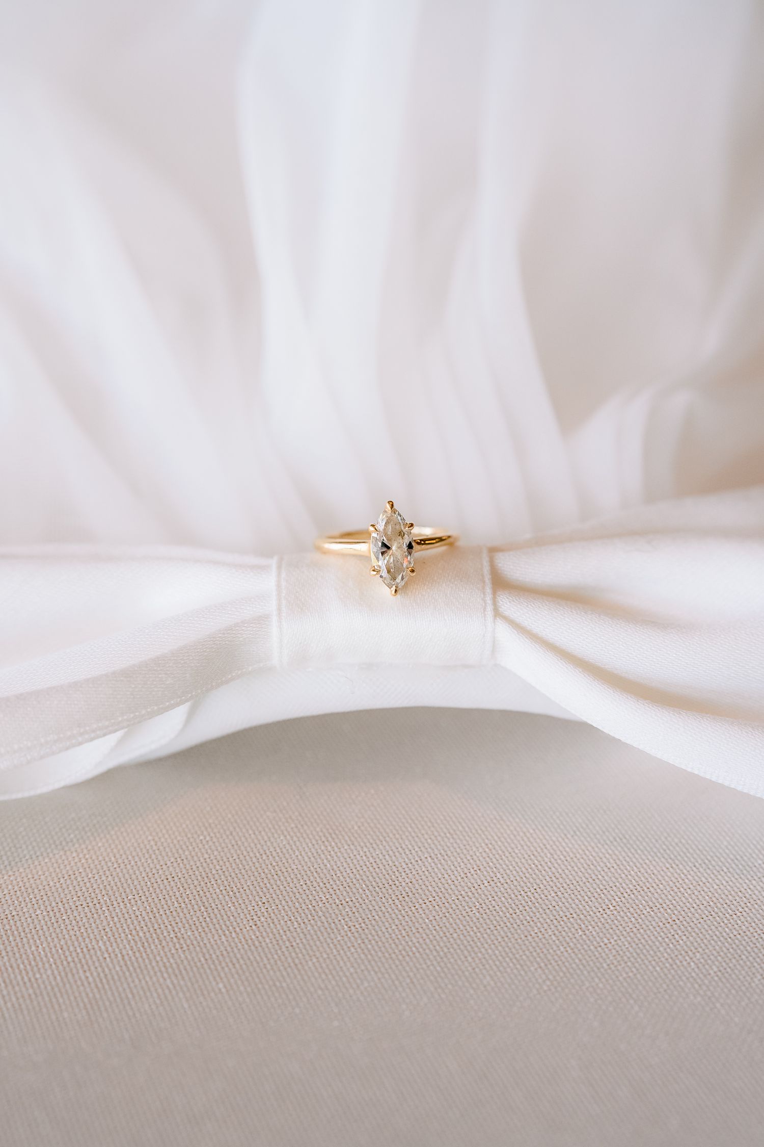 Gold marquise diamond engagement ring resting on white bridal veil fabric.