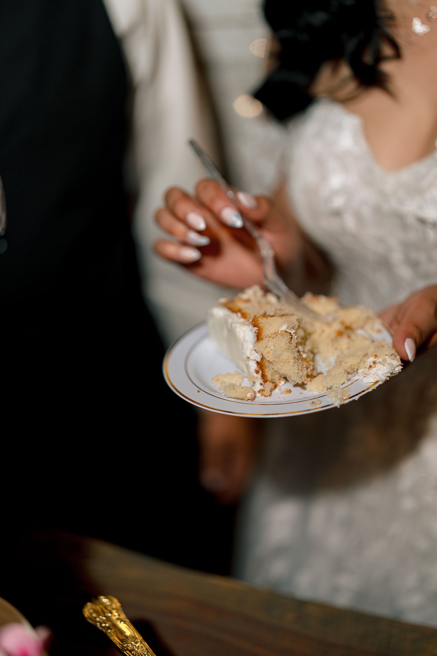 Bride and groom cutting wedding cake, holding white plate with slice of cake.