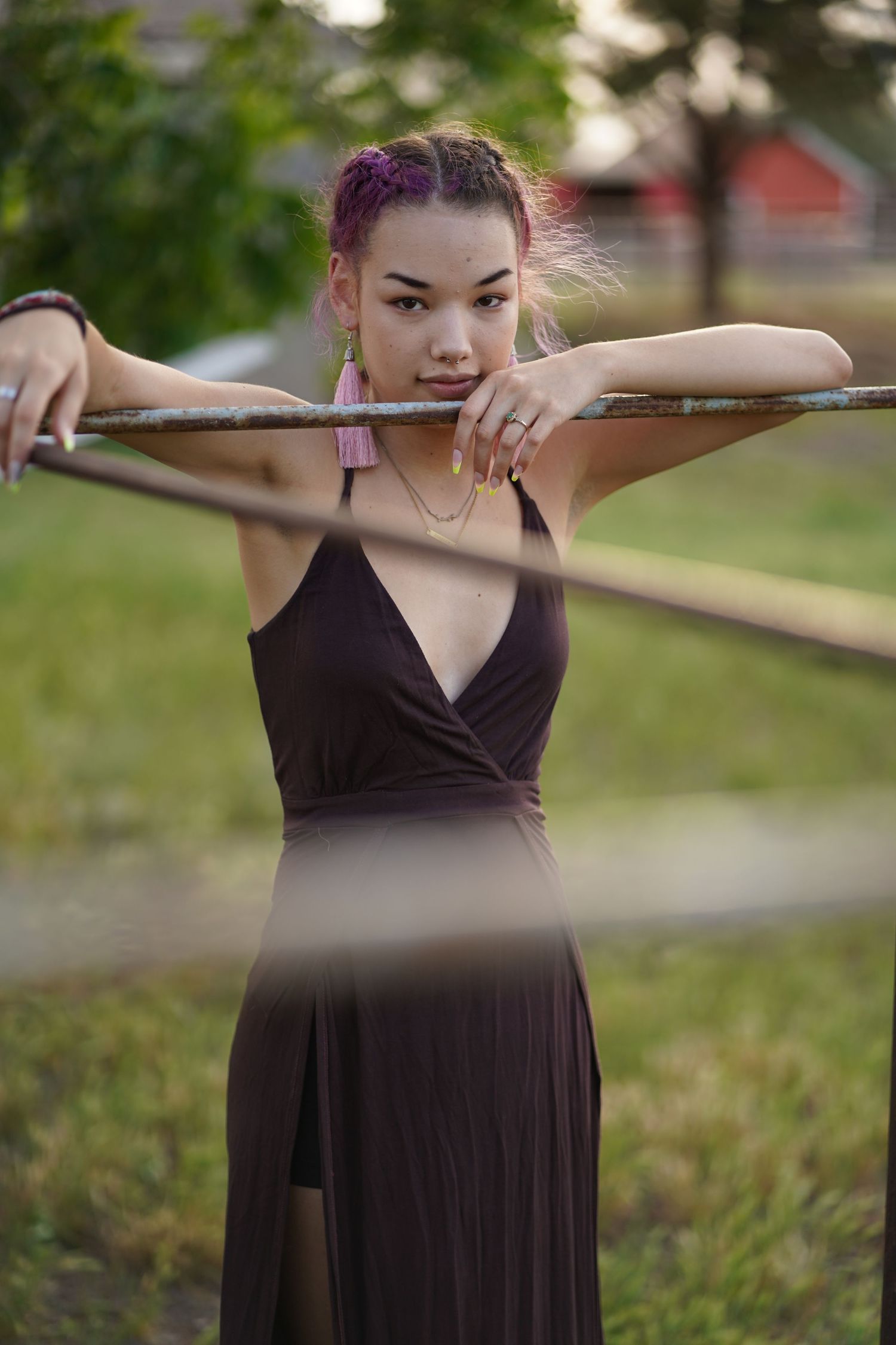 Person in black dress with pink hair leaning on wooden rail in outdoor setting.