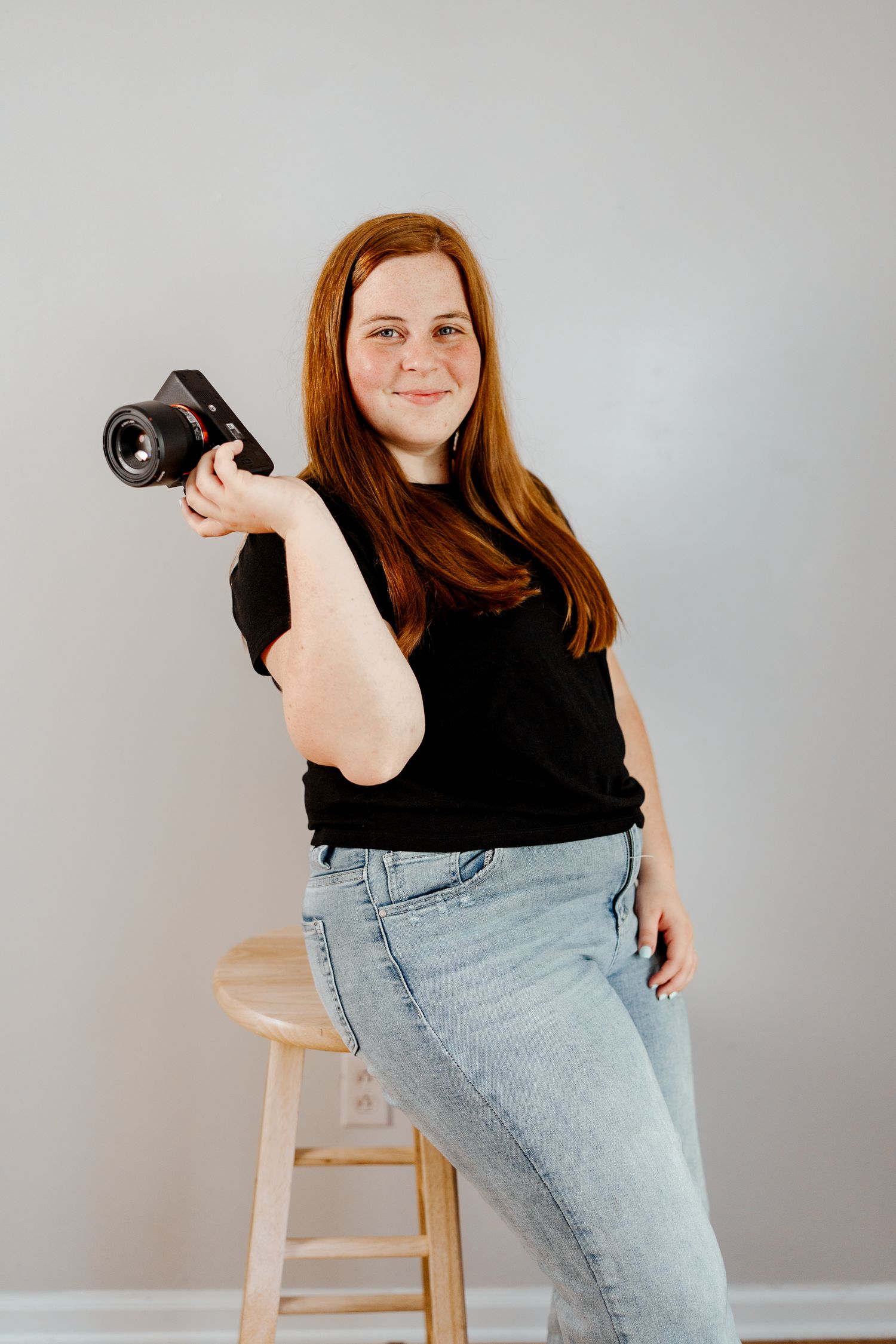 Person in black shirt holds camera while seated on wooden stool in creative poses.