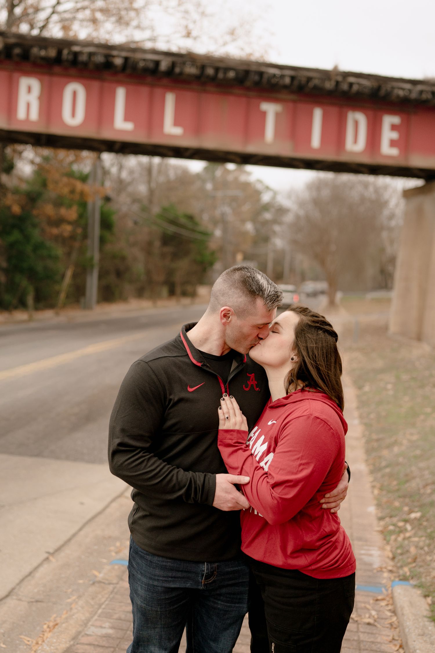 A couple shares a romantic kiss on a rural road during autumn while wearing coordinating red and black outfits.