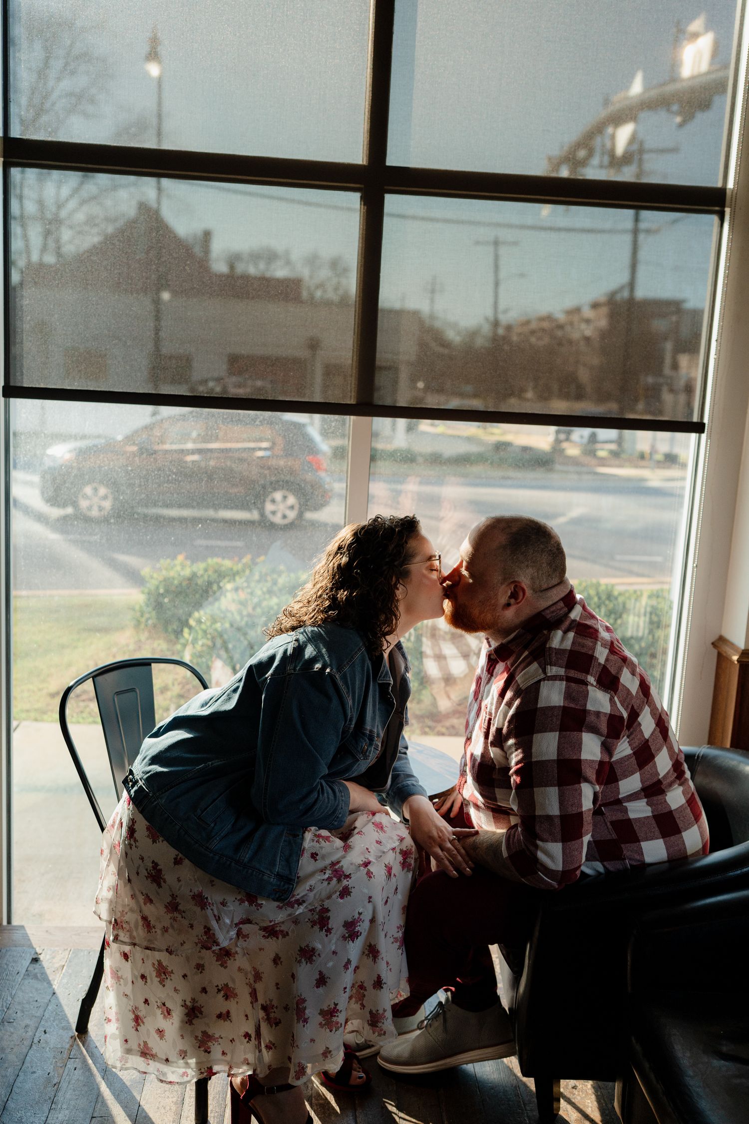 A couple sharing an intimate moment by a window in a restaurant booth during sunset.