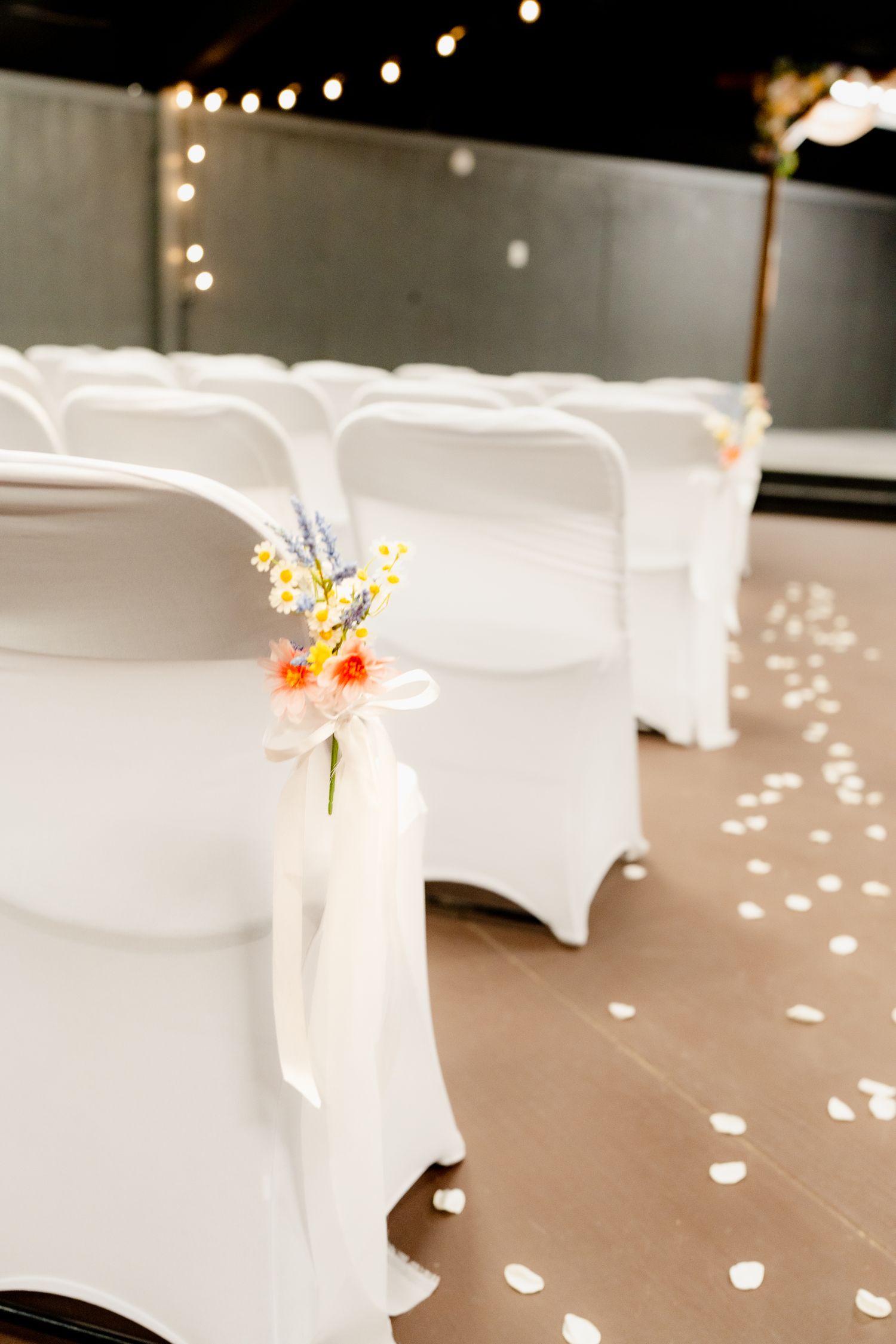 White chair covers with floral accents line a reception venue under twinkling string lights creating an elegant atmosphere.