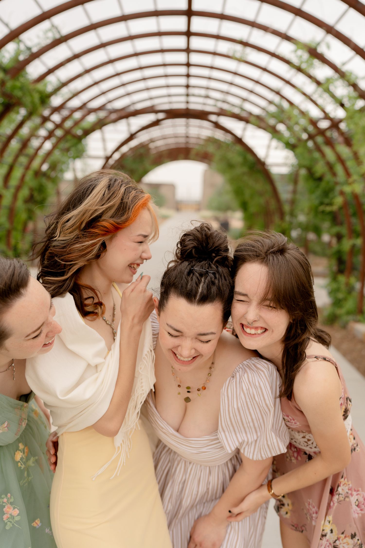 A group of friends share a joyful moment together in a greenhouse, leaning in close and laughing candidly.