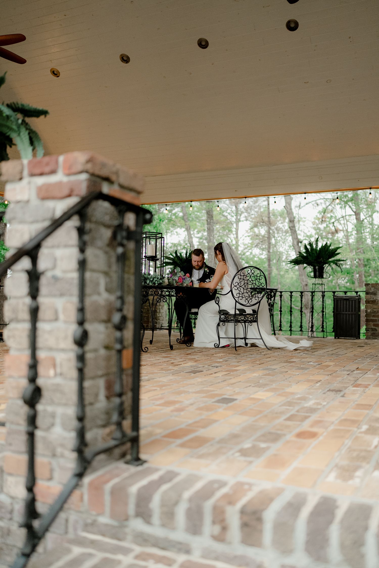 A bride and groom share a private moment on a brick patio with wrought iron furniture.