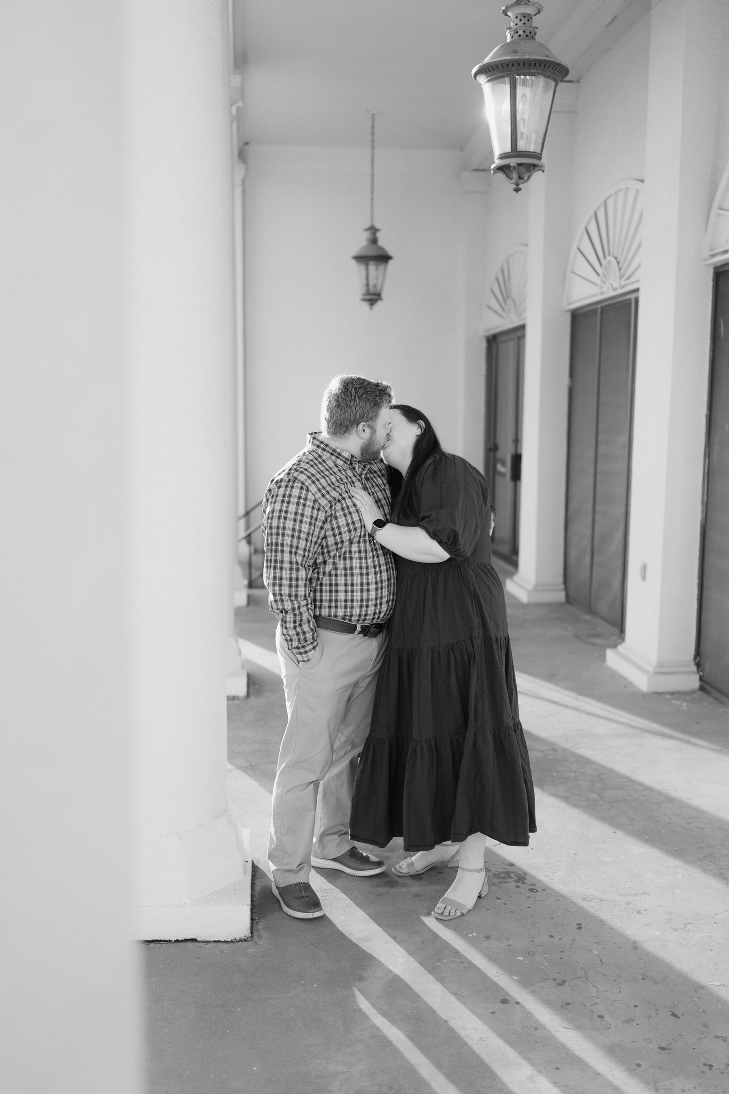 Black and white romantic photo of a couple sharing an intimate moment in a columned outdoor corridor.