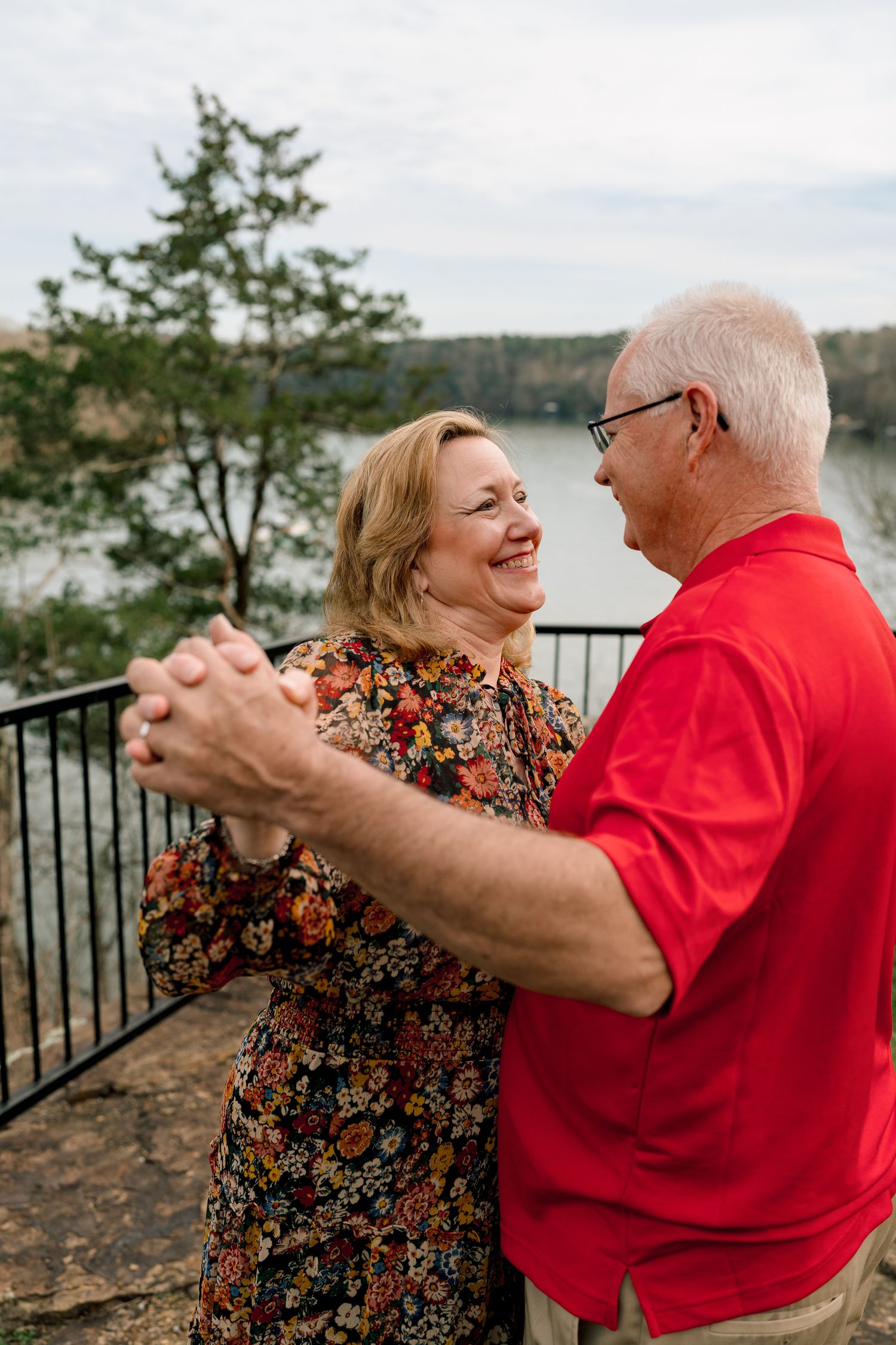 Joyful older couple dancing together on an overlook with a scenic lake and trees in the background.
