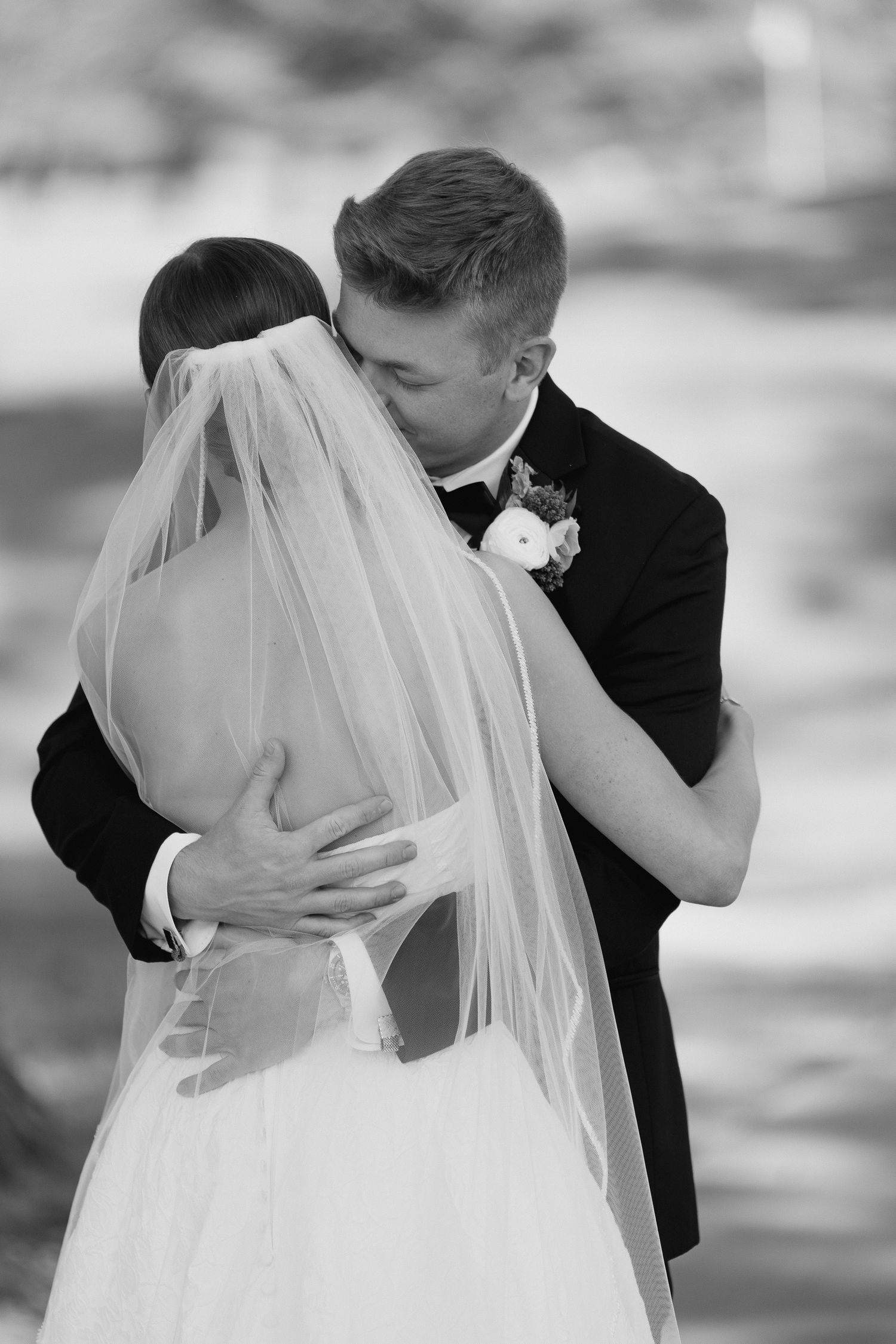 Black and white photo of a bride and groom sharing their first kiss, with her veil cascading down her back.