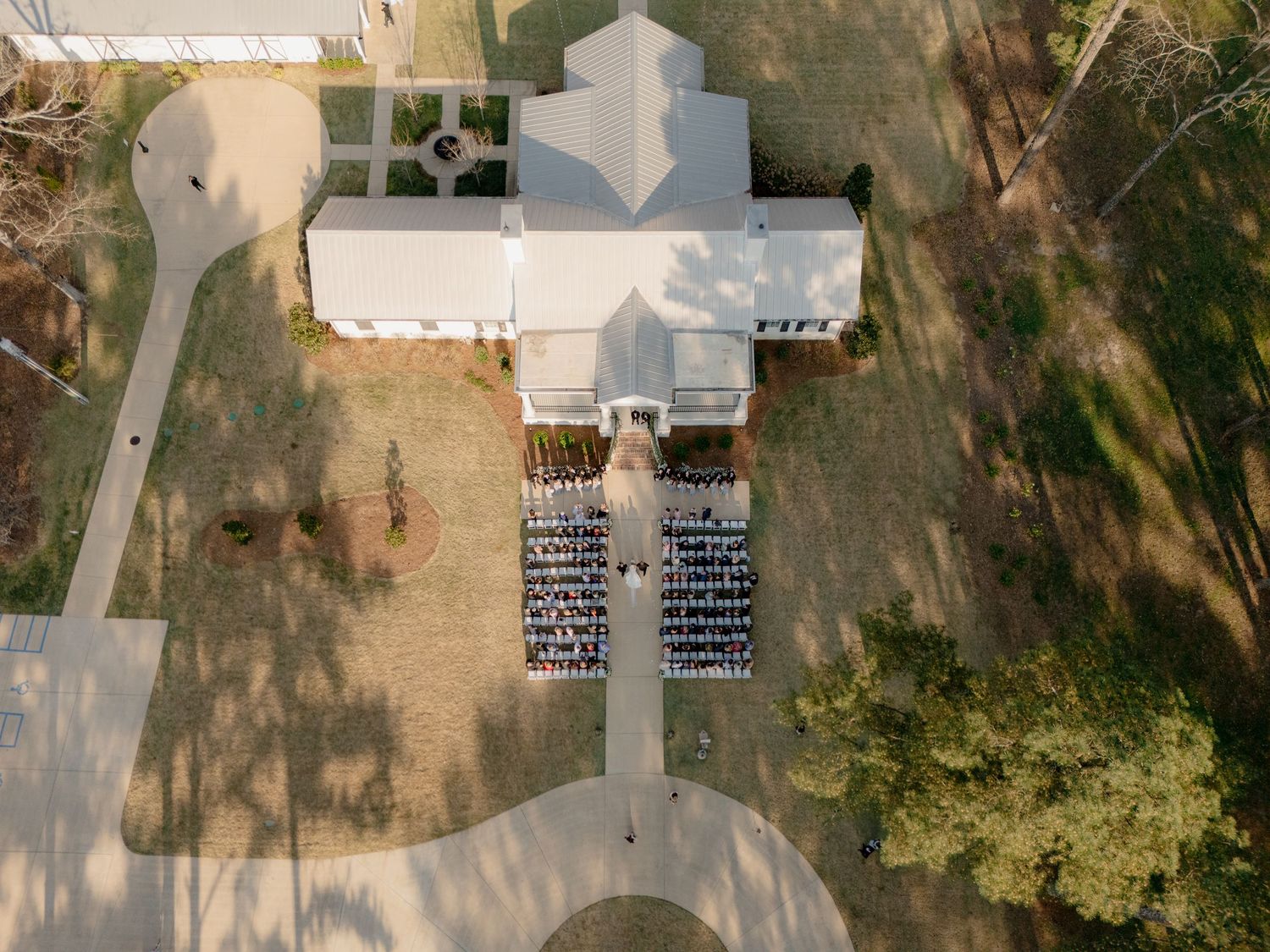 Aerial view of a white wedding venue with outdoor ceremony seating surrounded by trees and manicured grounds.