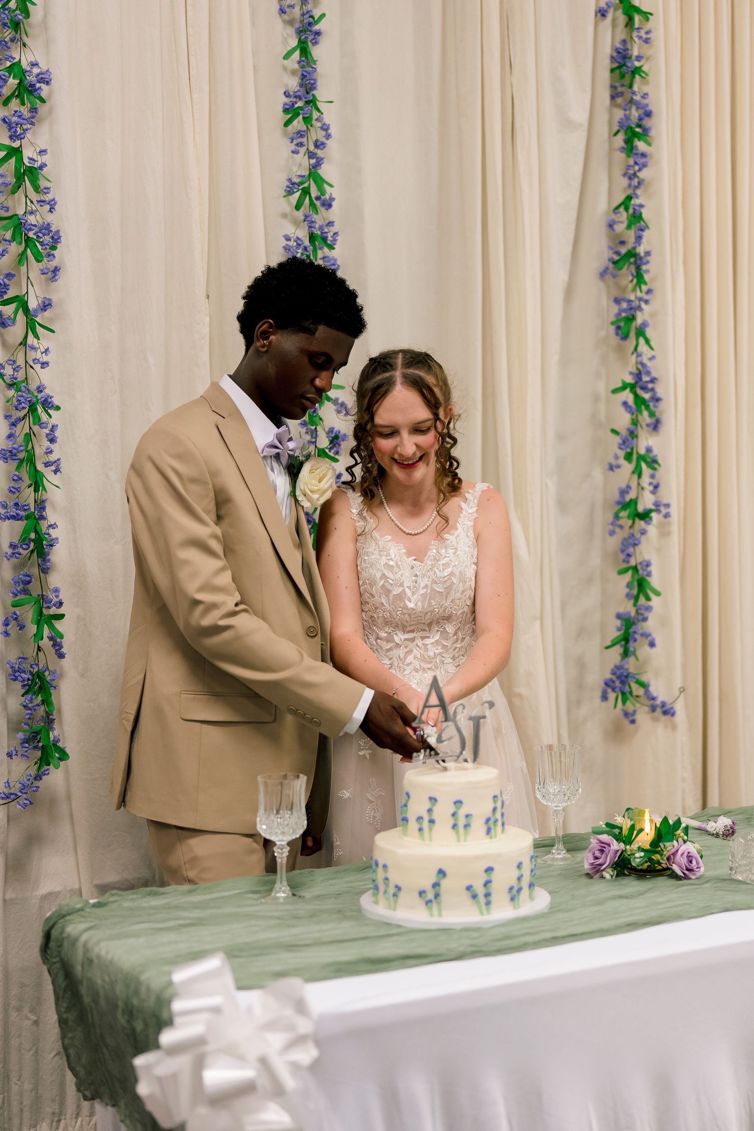 Interracial couple cuts their two-tier white wedding cake at their reception.