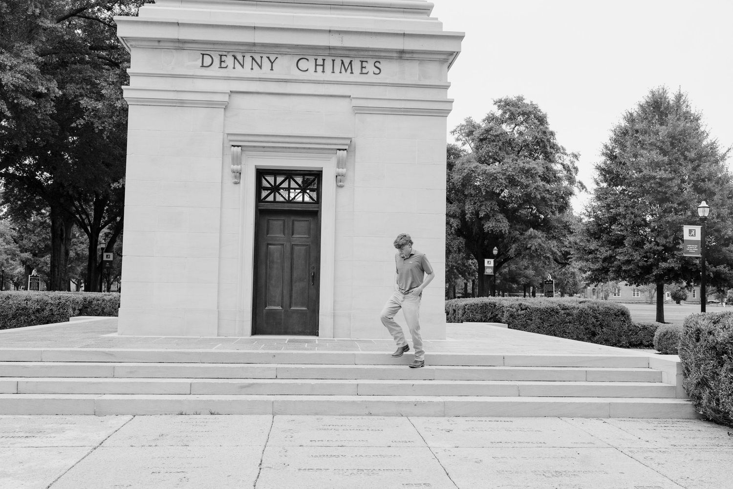 Black and white photo of person posing on the steps of Denny Chimes building.