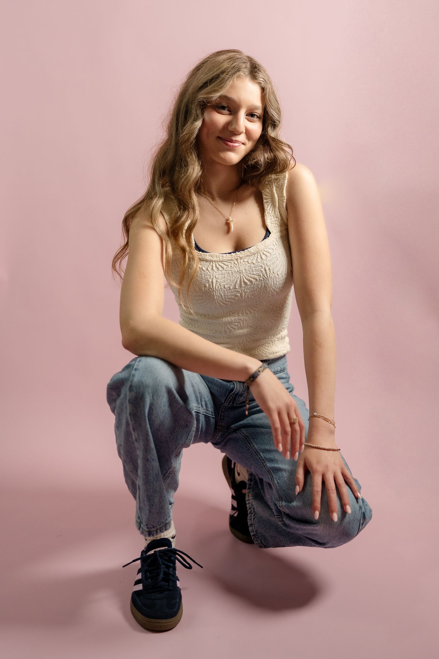 Casual fashion portrait with relaxed denim and cream top against pink studio background.