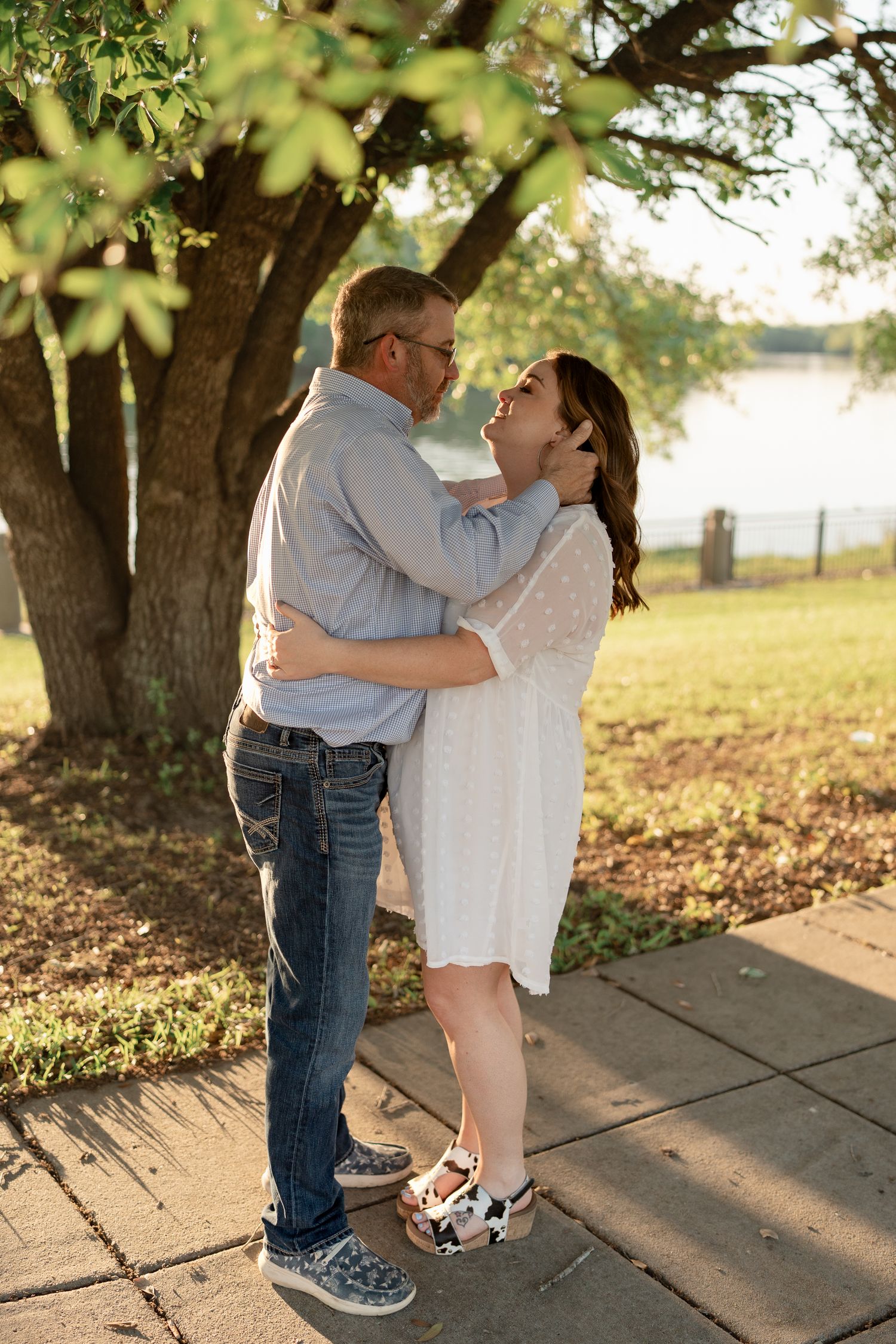 Romantic couple embracing under a tree during golden hour sunset by a lake.