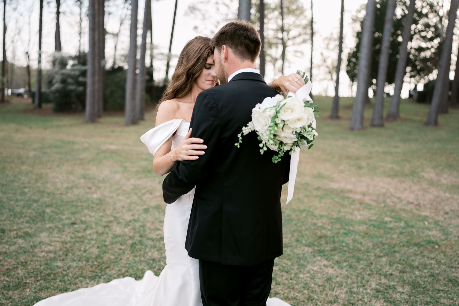 Newlyweds embrace in intimate moment outdoors with white bouquet.