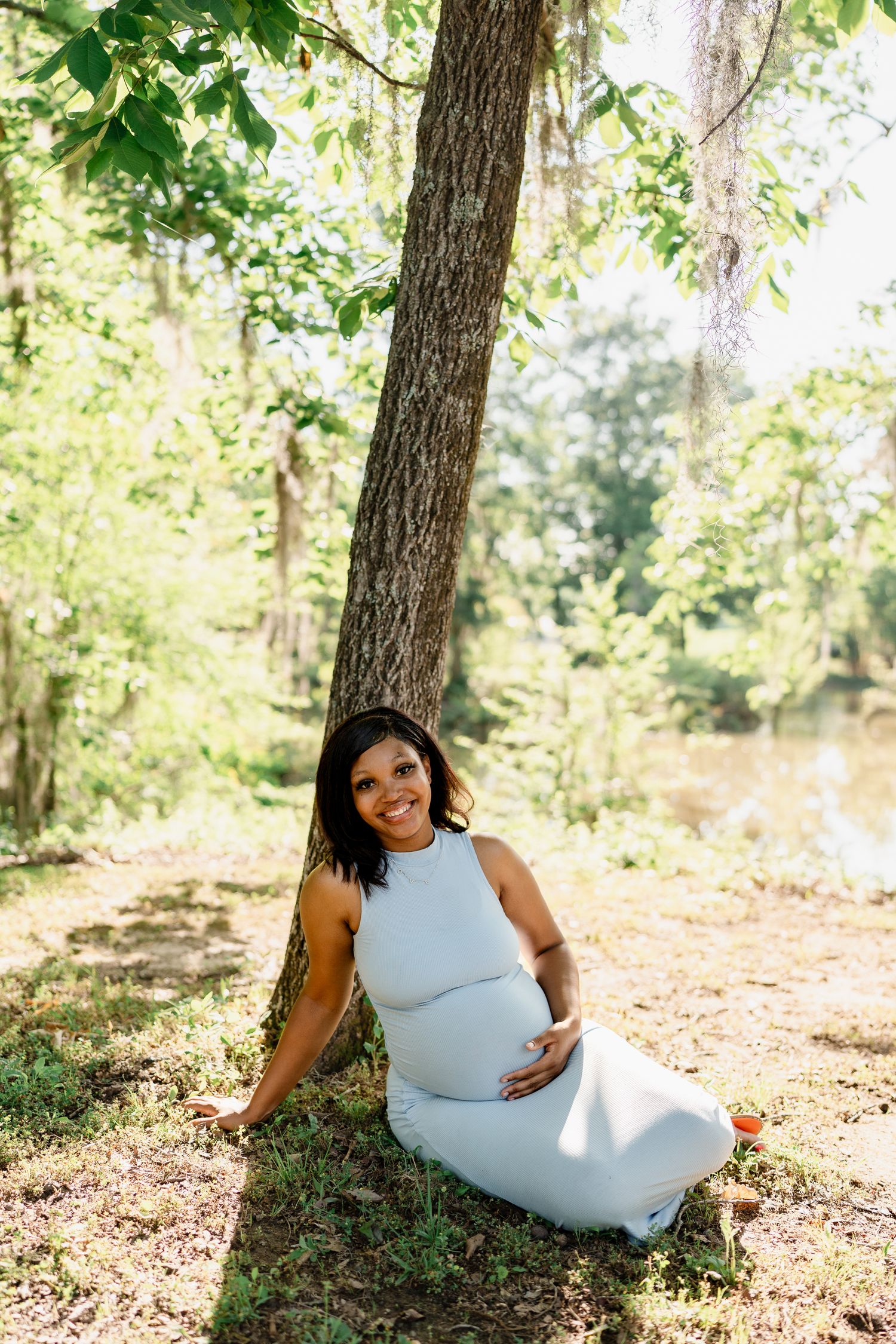 Maternity photo of woman in blue dress reclining on forest floor.