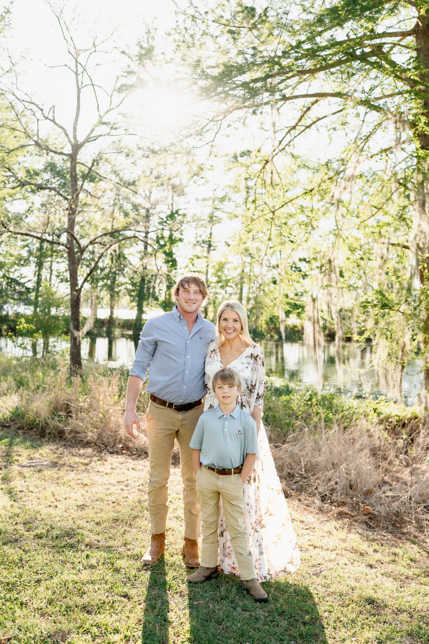 Sunlit family portrait session in wooded area with natural spring foliage.