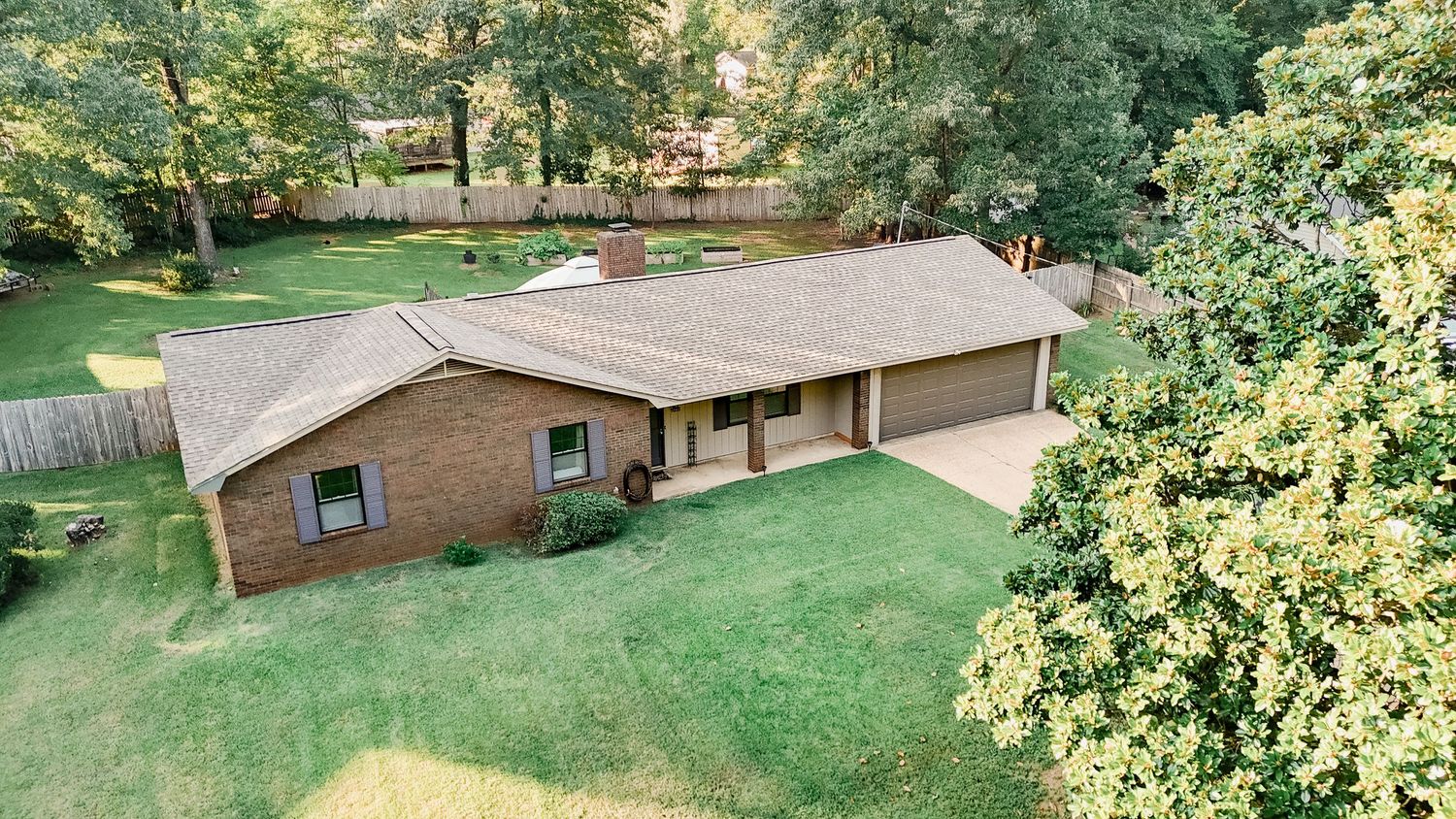 Panoramic view of a spacious backyard with lush green lawn, trees, and brick ranch-style home in natural sunlight.