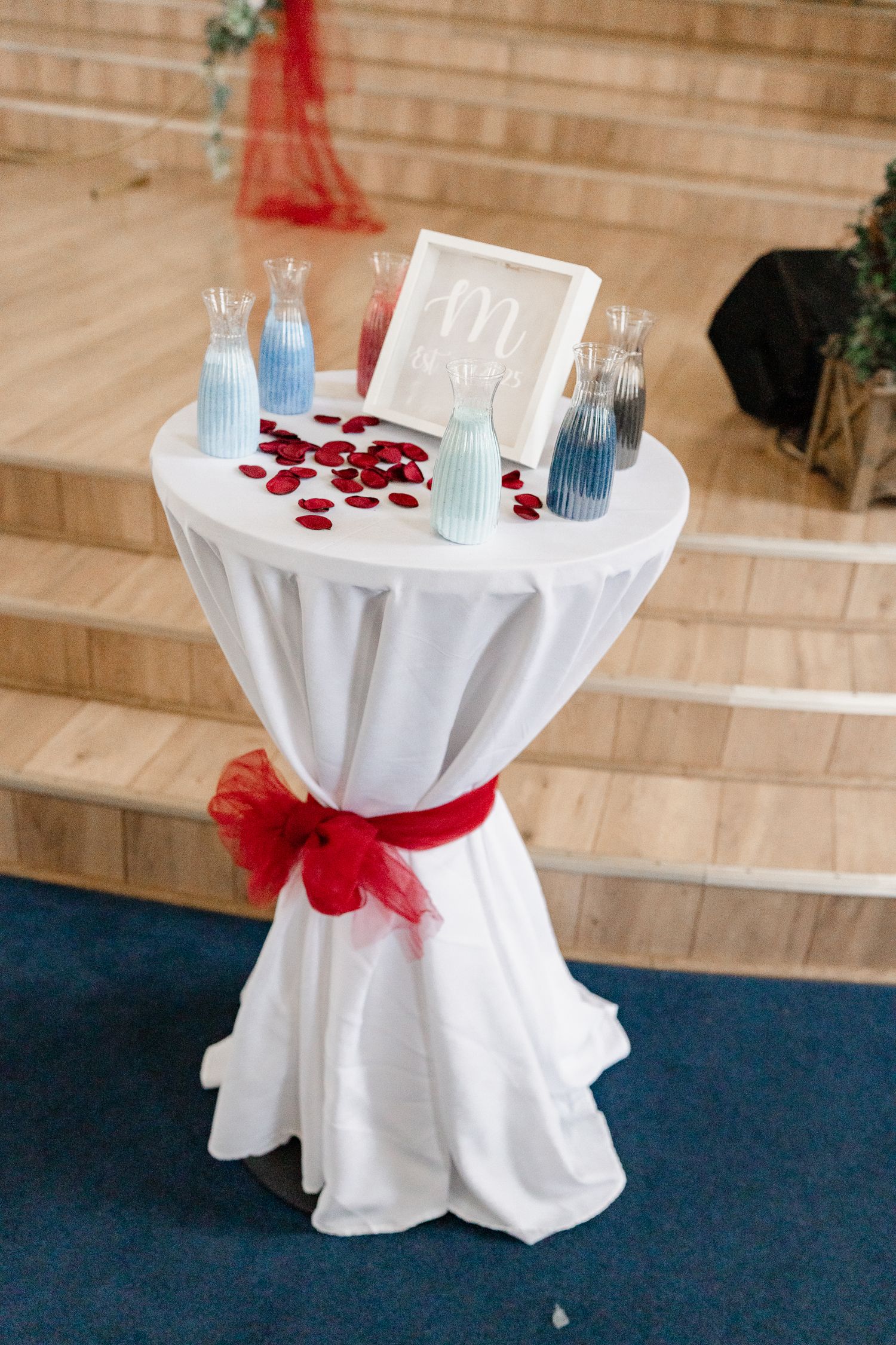 White cocktail tables with red accents and blue vases arranged for an event.