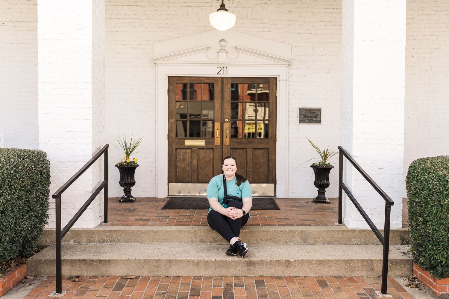 Person sitting on white-columned entrance steps with ornate wooden door and black railings.