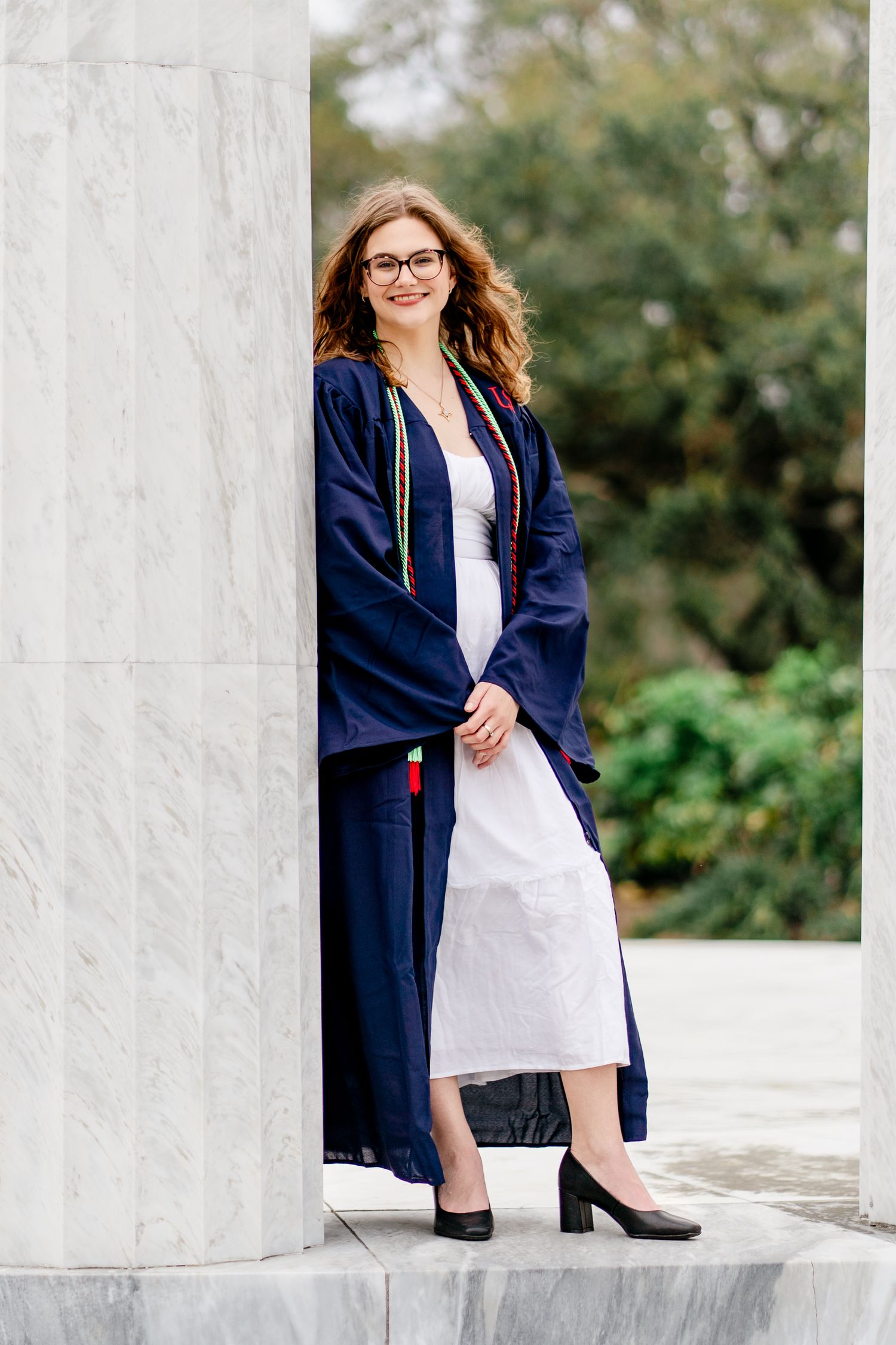Graduate poses elegantly between white marble columns for graduation photos.