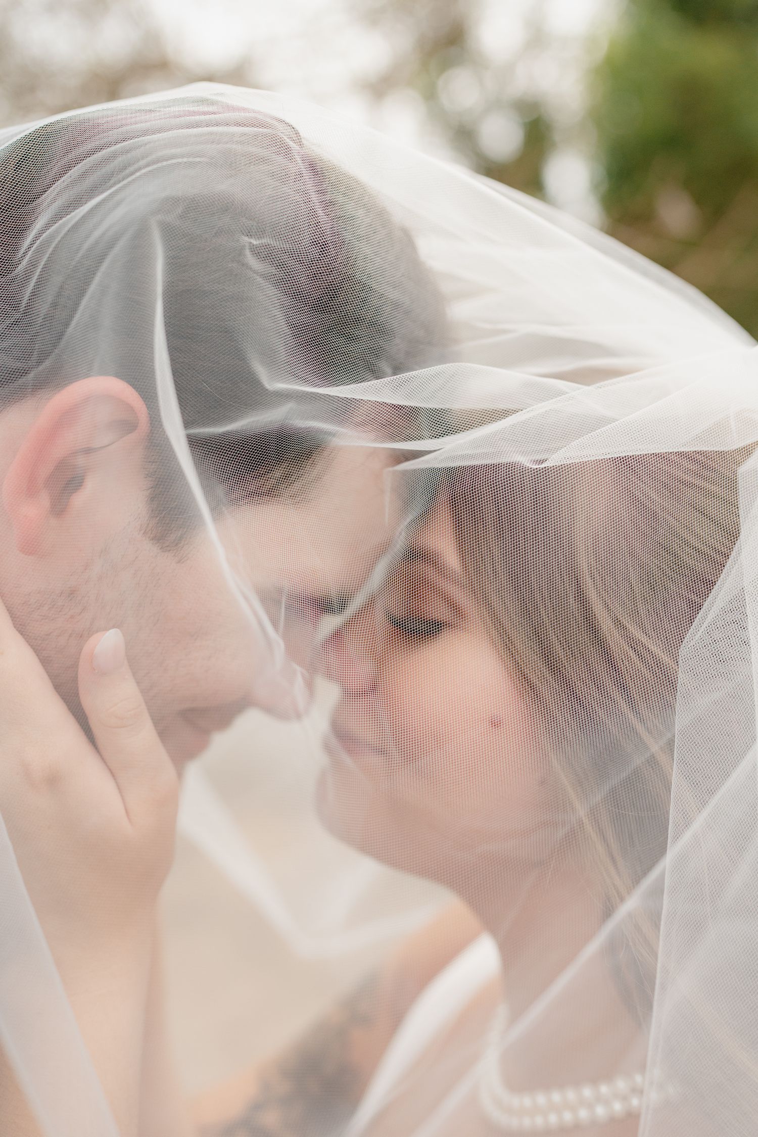 A romantic wedding portrait shows a couple sharing an intimate moment under a flowing white veil.