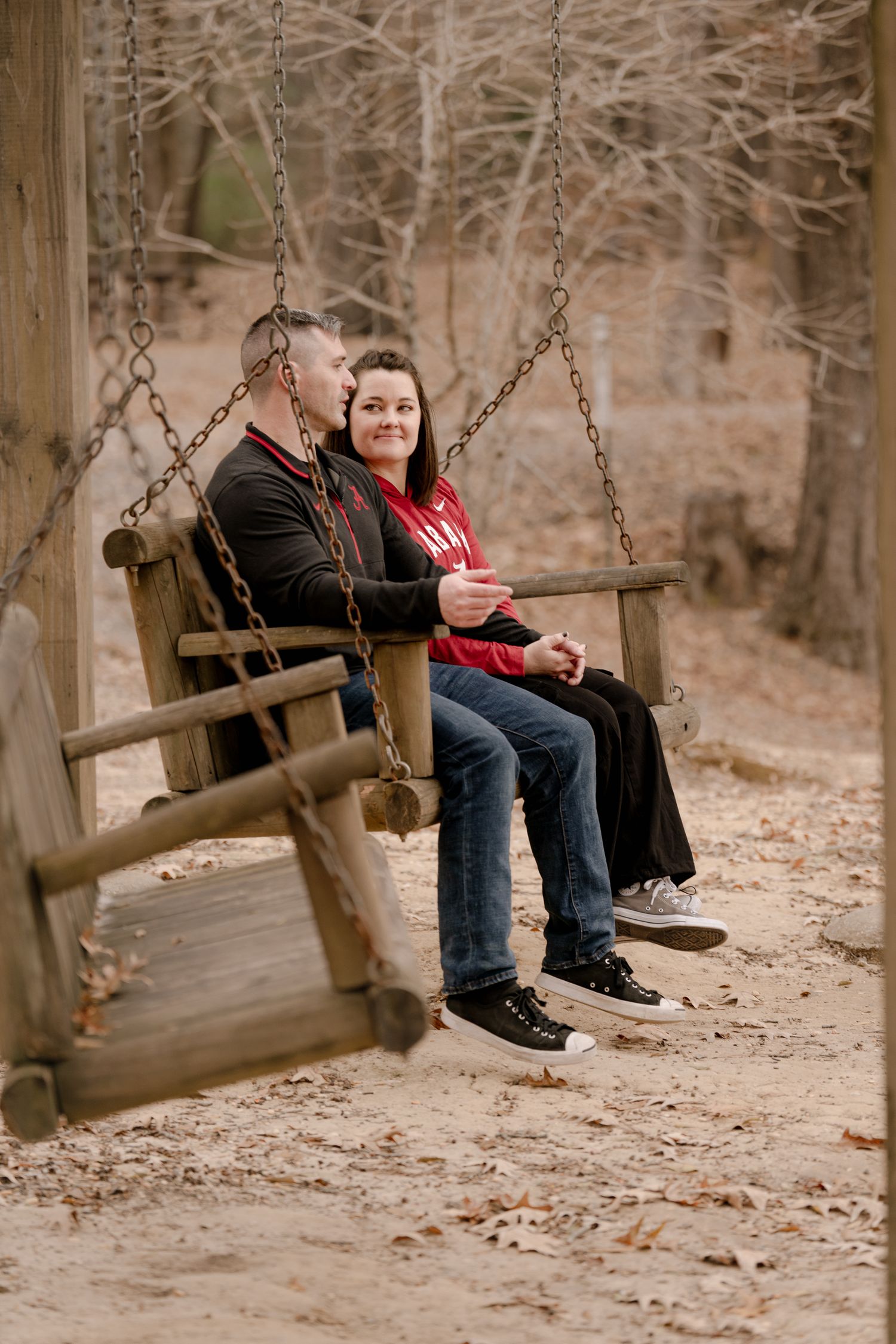 Two people sit together on wooden swings in an autumn park setting.