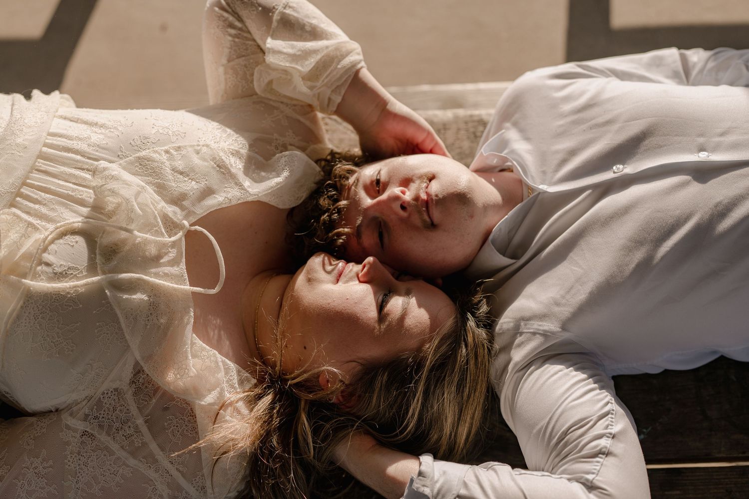 Romantic couple lying down together, faces close, bathed in warm sunlight.