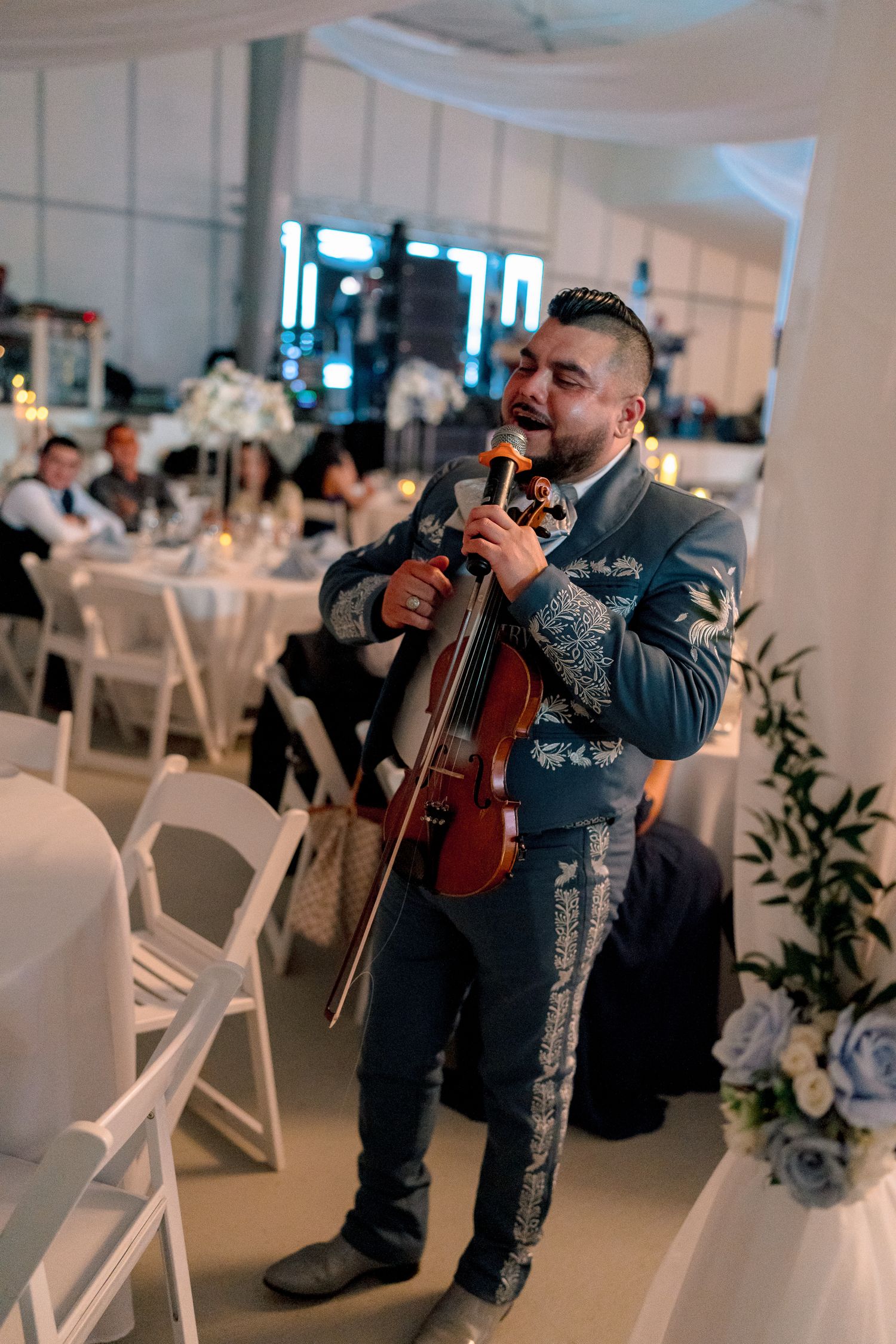 A mariachi musician in traditional attire performs with a violin at an indoor wedding reception.