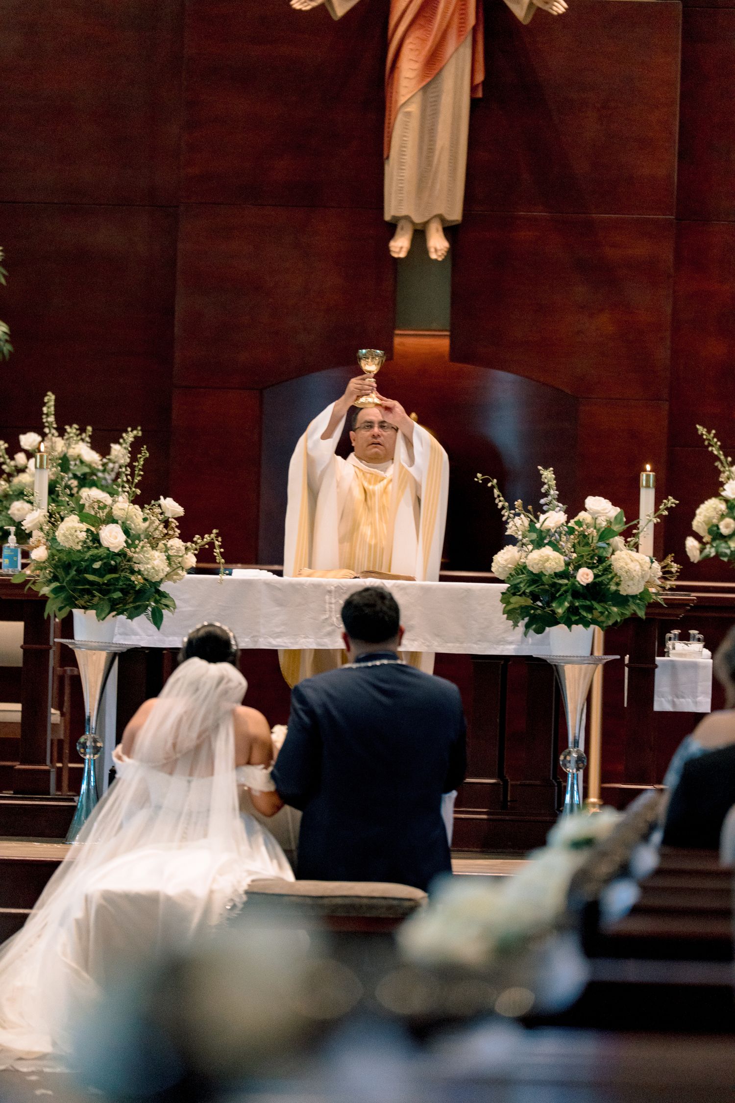 A wedding ceremony in progress at a church altar with white floral arrangements and elegant decor.