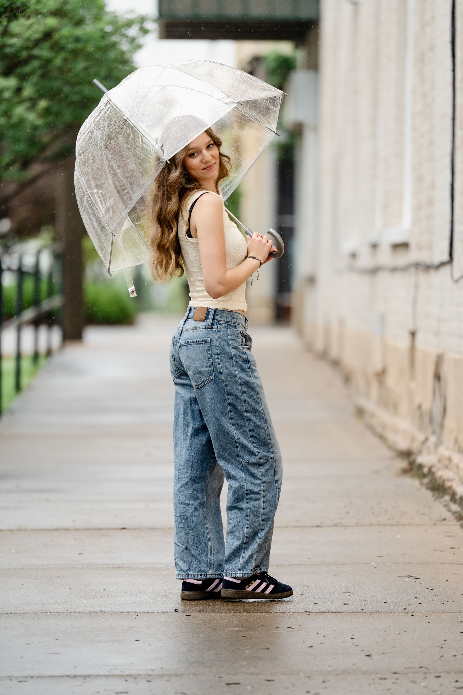 Clear umbrella fashion photography on urban sidewalk with architectural details.