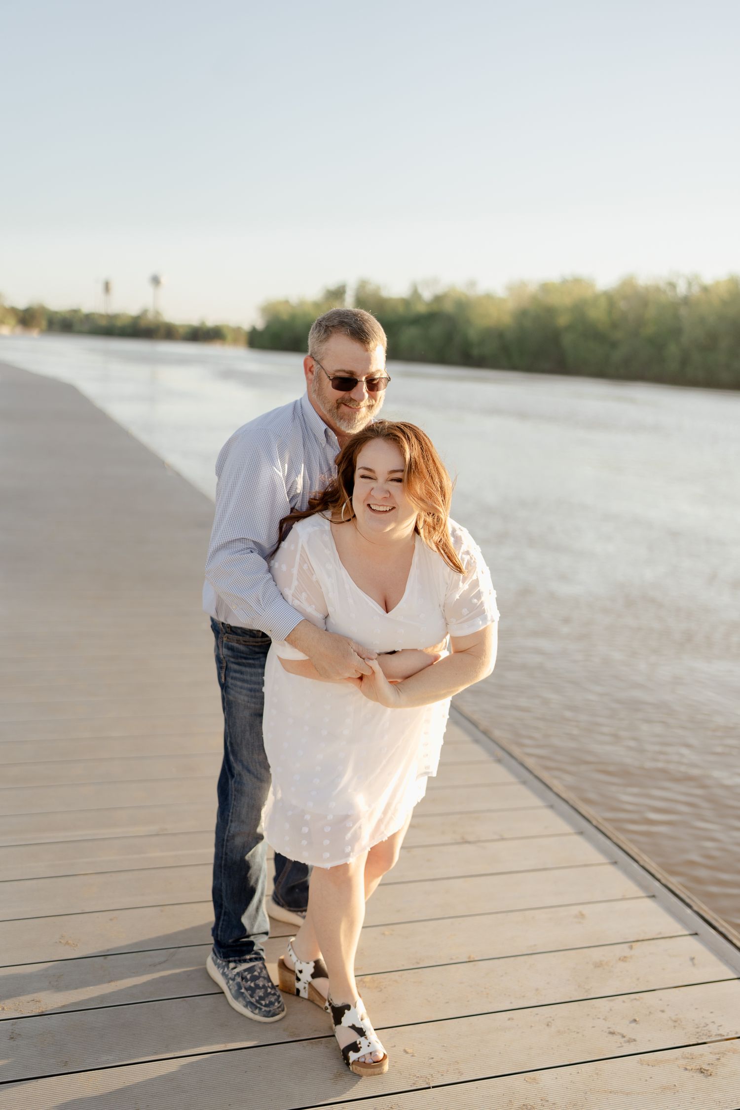 Two people share a playful moment while walking on a waterfront boardwalk.