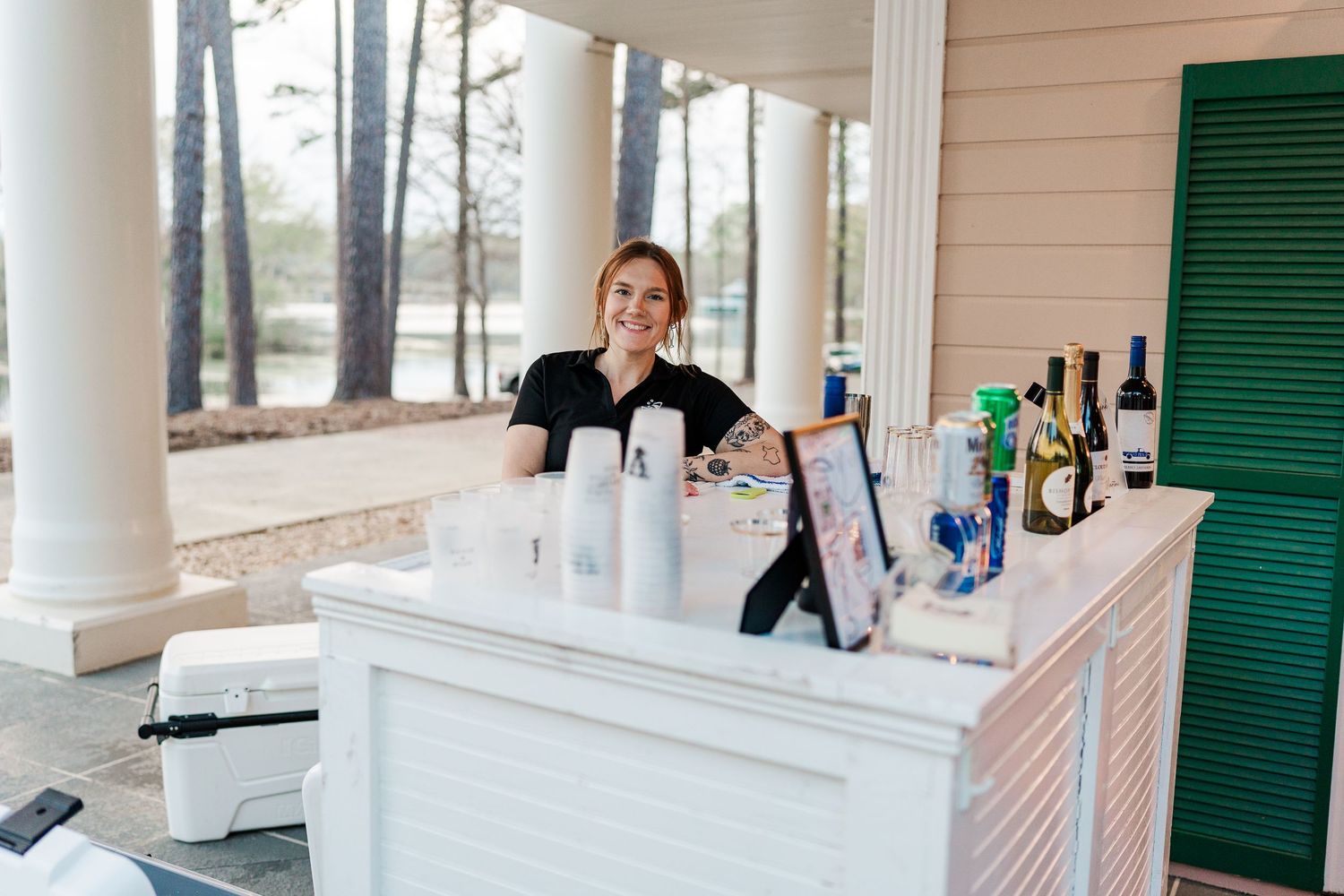 Professional bartender standing behind a white outdoor bar setup with bottles and supplies.