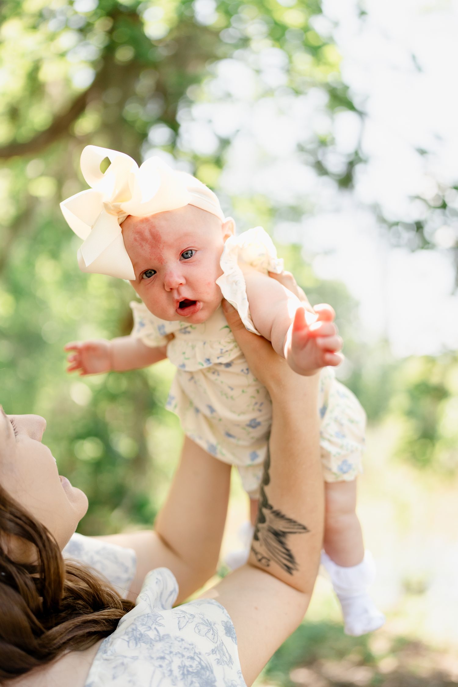A delightful outdoor photoshoot featuring a baby being lifted in the air against a sunny forest backdrop.