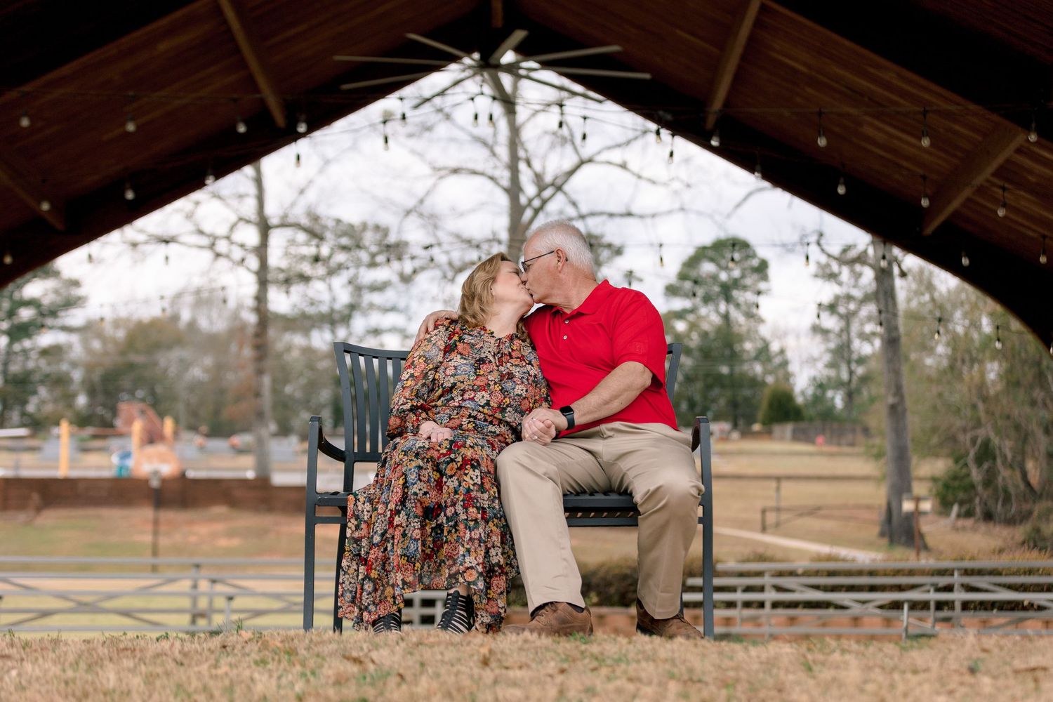 Romantic older couple sharing a kiss on a bench under a gazebo with string lights.