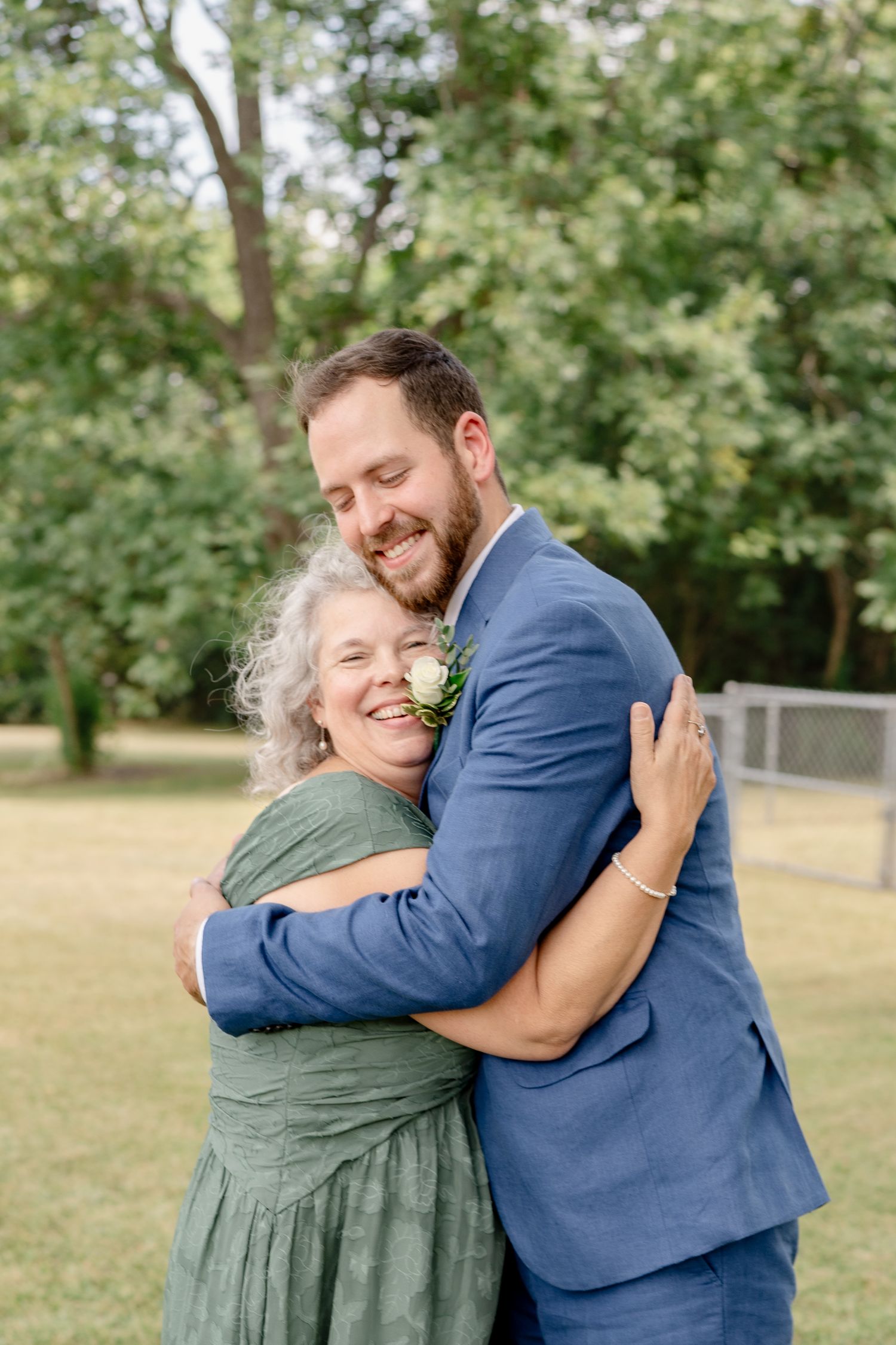 A heartwarming embrace between two people on a sunny day with green trees in the background.