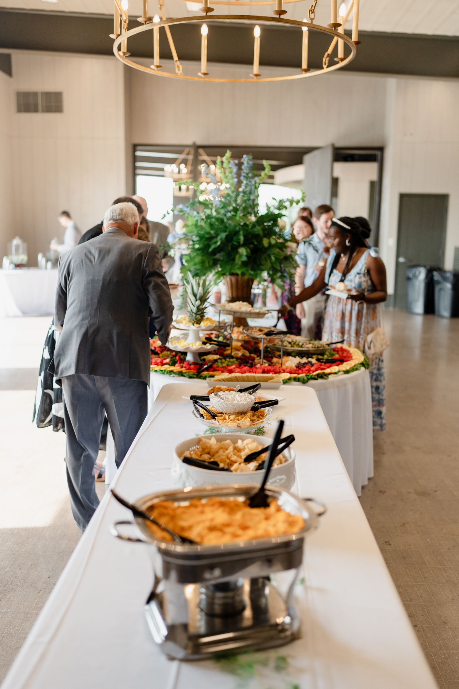 Long white buffet table with chafing dishes and serving stations set up for a wedding reception.