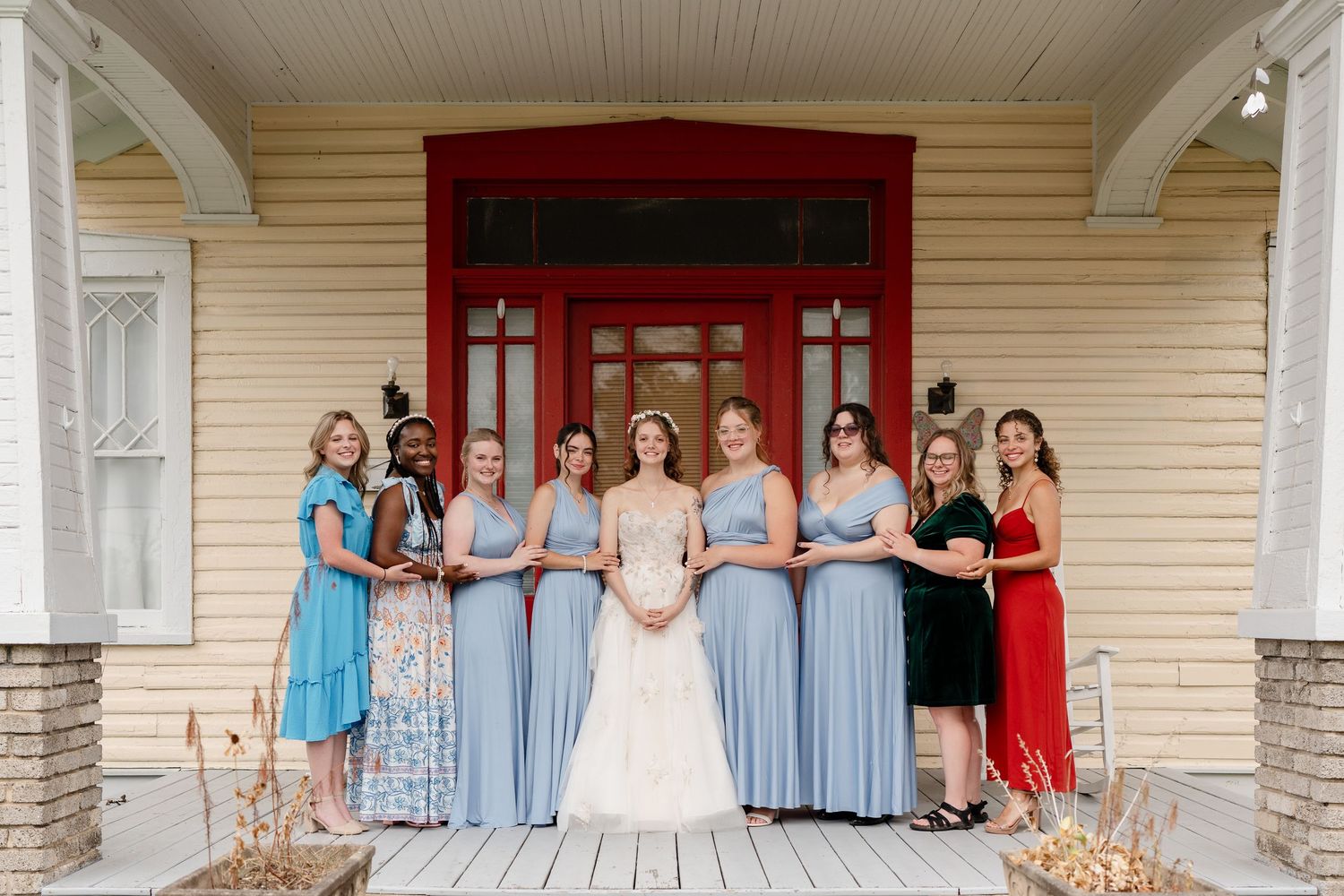Wedding party members in light blue bridesmaid dresses and formal attire pose together on a covered porch.