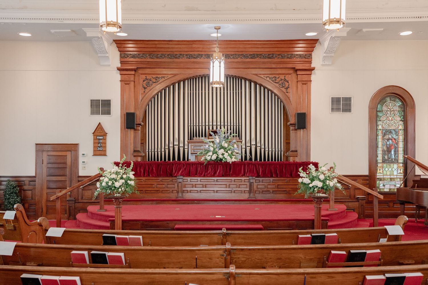 Church sanctuary with wooden pews, arched ceilings, and ornate organ pipes arranged in symmetrical layout.