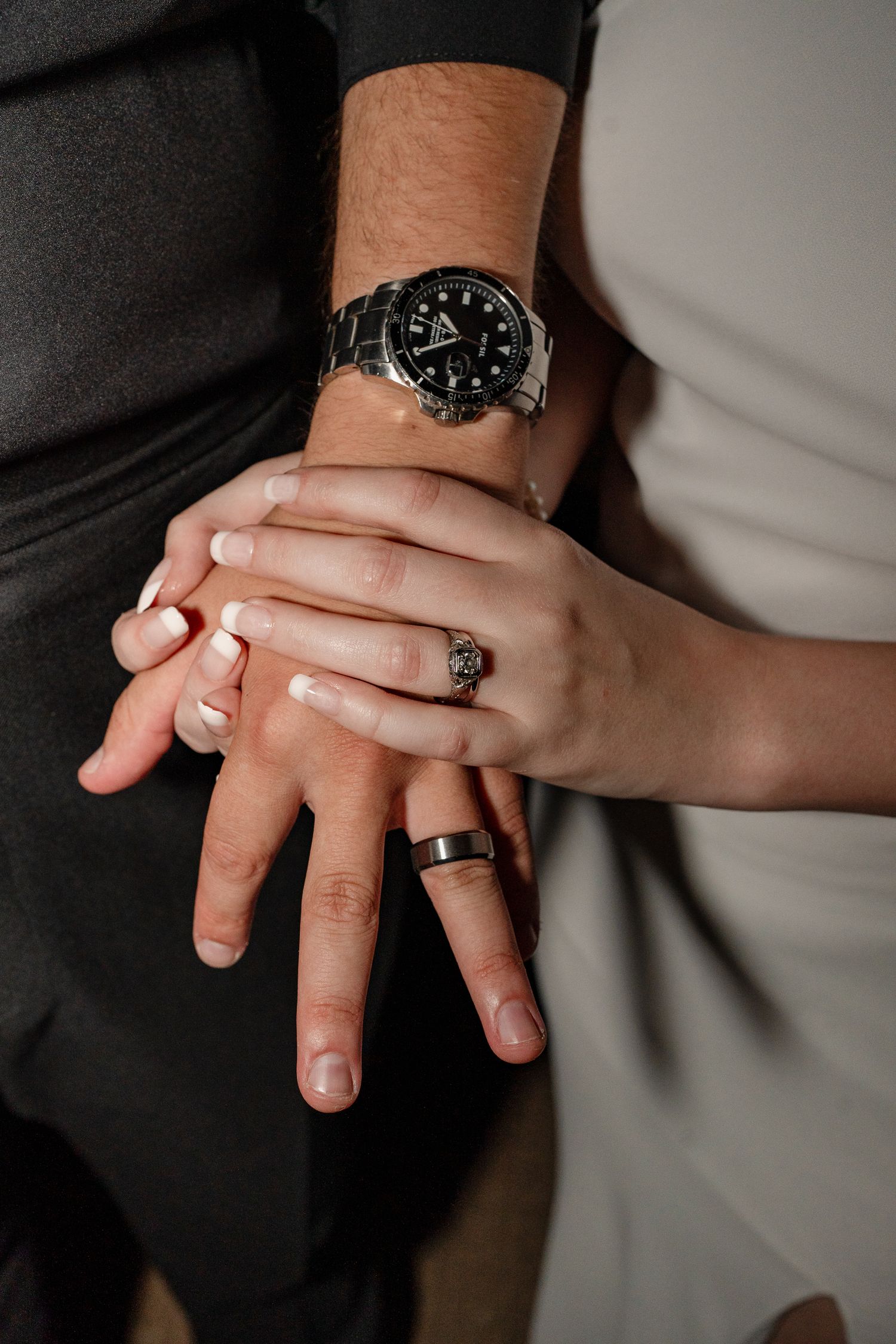 Close-up of hands showing wedding rings and a black watch against formal attire.
