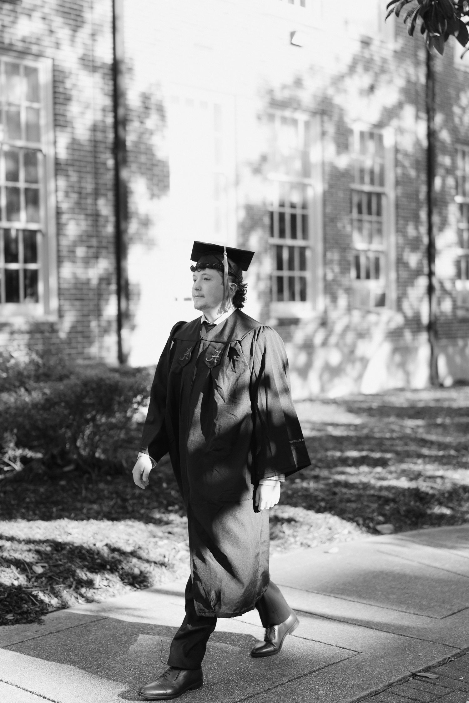 A graduate in cap and gown walks confidently on a campus pathway in this classic black and white graduation portrait.